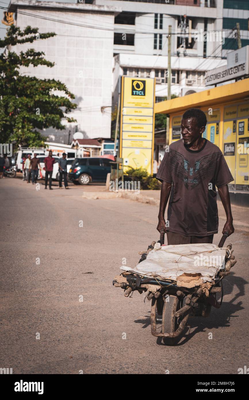 25.03.2022 - Mwanza, Tansania - einheimischer afrikanischer Mann, der einen Wagen in den belebten Straßen schiebt Stockfoto