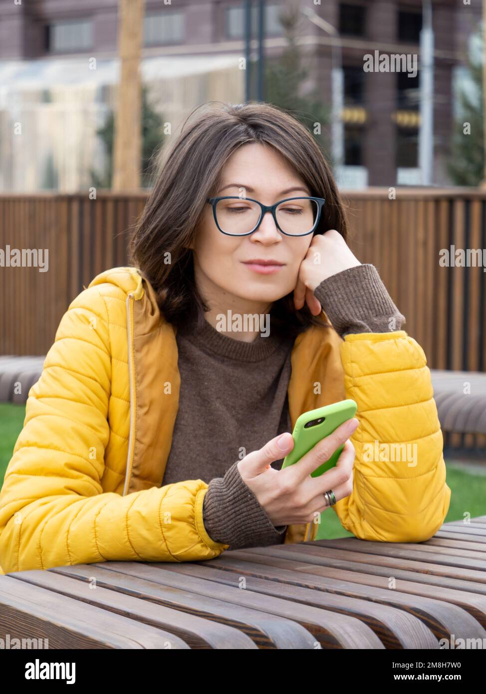 Eine Frau mit Brille liest Nachrichten oder Nachrichten auf ihrem Smartphone. Einsatz von Wireless-Technologien im Freien. Urbaner Lebensstil. Stockfoto