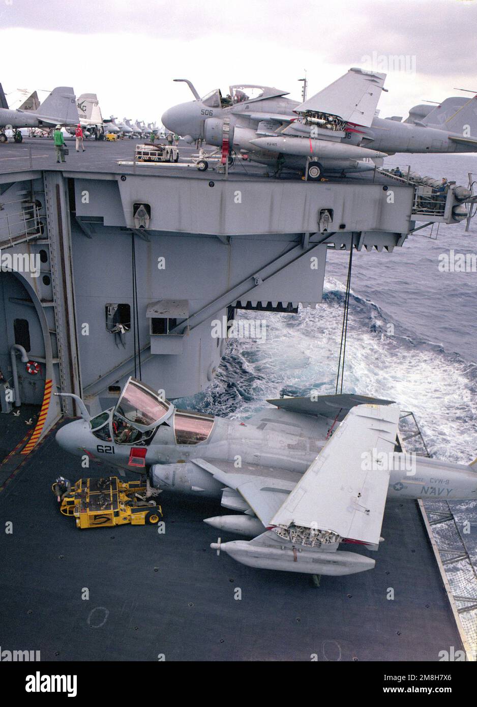 Ein Besatzungsmitglied, das ein SD-1D-Flugzeug betreibt und einen Dolly beobachtet, positioniert ein taktisches elektronisches Kriegsgeschwader 138 (VAQ-138) EA-6B Prowler-Flugzeug in einem Aufzug des nukleargetriebenen Flugzeugträgers USS NIMITZ (CVN-68). Land: Pazifik (POC) Stockfoto