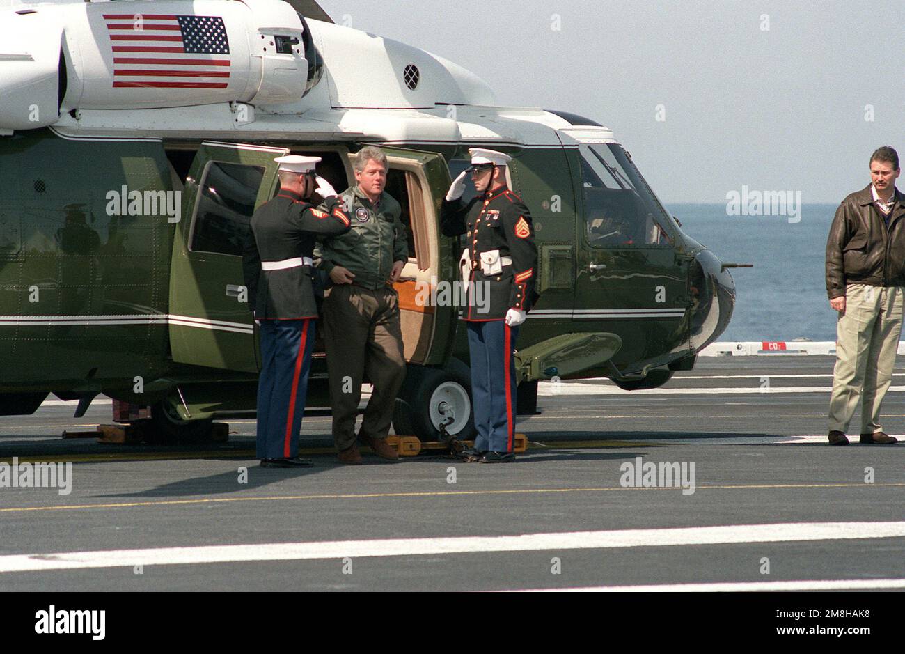 Marines salutieren, wenn Präsident William Jefferson Clinton mit dem Marine Helicopter Squadron 1 (HMX-1) VH-60 Sea Hawk Helikopter an Bord des nuklearbetriebenen Flugzeugträgers USS Theodore Roosevelt (CVN-71) eintrifft. Clinton und der Verteidigungsminister Les Aspin besuchen die Fluggesellschaft, die vor der Küste von Norfolk, VA, unterwegs ist. Land: Atlantik (AOC) Stockfoto