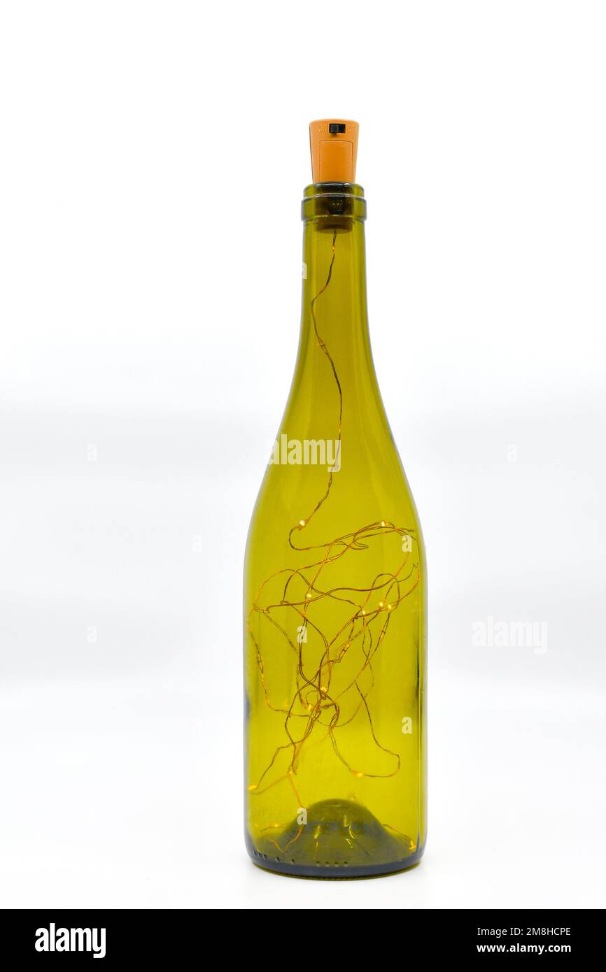 Hohe grüne Weinflasche gefüllt mit dünnen Drähten und LED-Feenlicht als Tischschmuck, isoliert auf weißem Hintergrund. Stockfoto