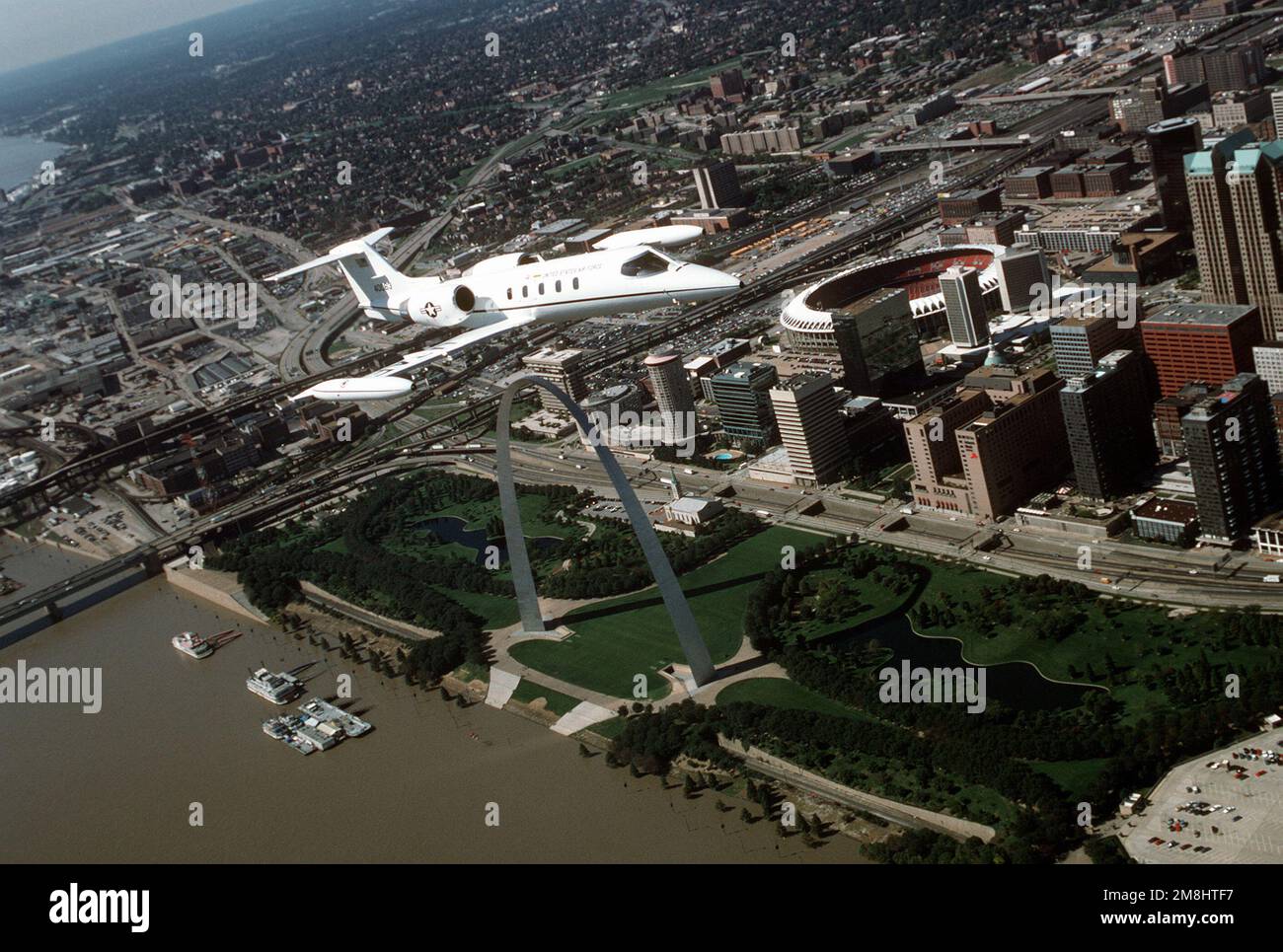 Ein dreiviertel-Vorderansicht eines von Lear Jet gebauten C-21A-Flugzeugs während eines Fluges über den berühmten St. Louis Arch, am Ufer des Mississippi River und im Busch-Stadion. Die C-21A ist dem 375. Airlift Wing, Air Mobility Command, zugewiesen. Stützpunkt: Luftwaffenstützpunkt Scott Bundesstaat: Illinois (IL) Land: Vereinigte Staaten von Amerika (USA) Stockfoto