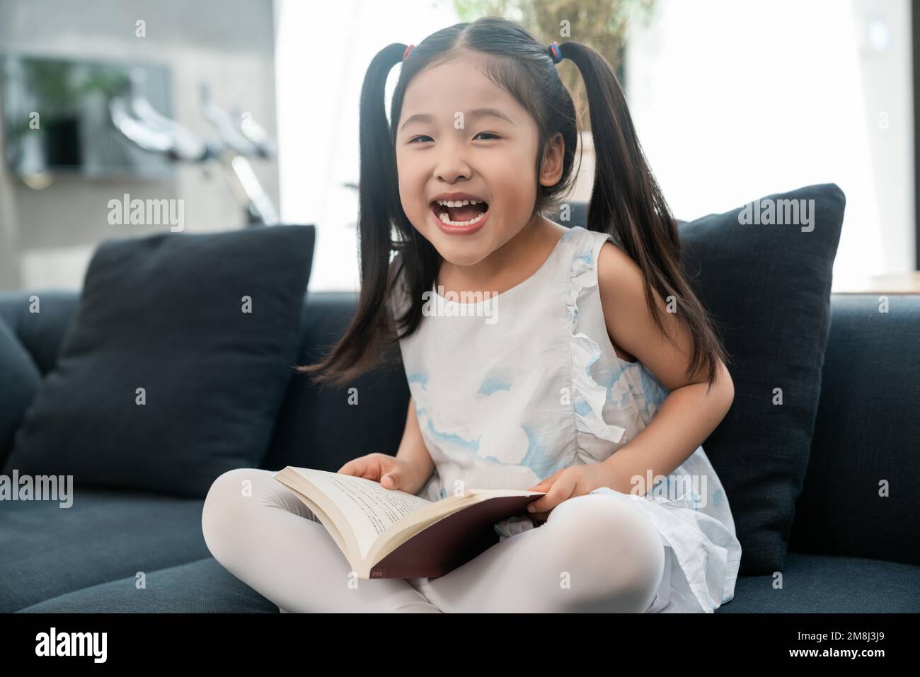 Das kleine Mädchen auf dem Sofa, das ein Buch liest Stockfoto