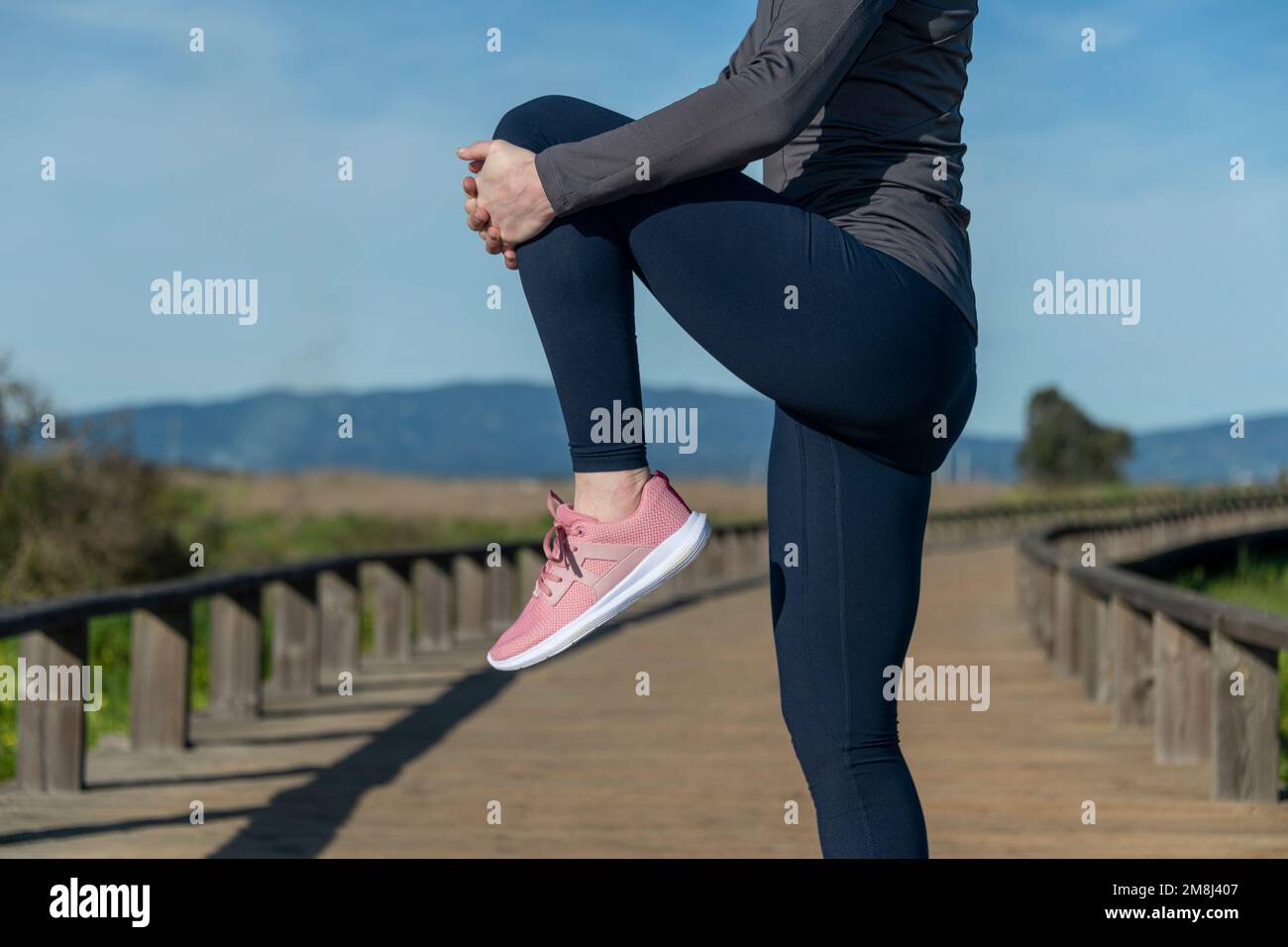 Beindehnung Training Trainingläuferin beim Laufen Warm-Up, dehnen sich die Oberschenkelmuskeln im Stehen mit einem Knie bis zur Brust. Stockfoto