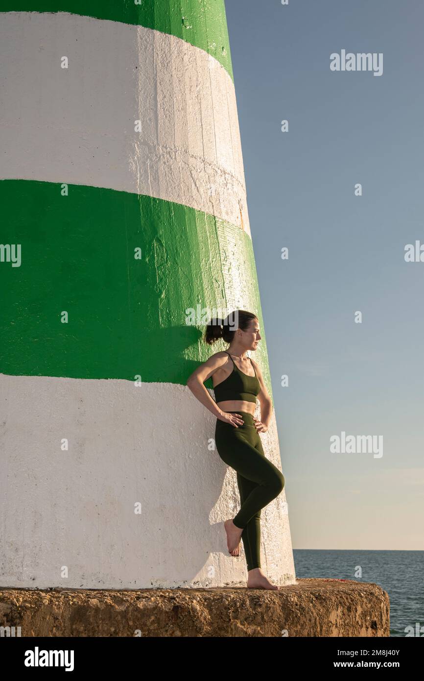 Sportliche Frau, die sich nach dem Training gegen einen Leuchtturm lehnt. Stockfoto