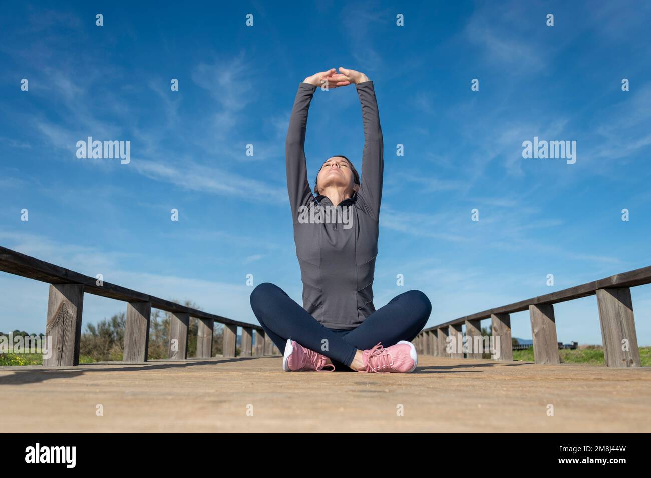 Sportliche Frau, die mit gekreuzten Beinen sitzt und eine Übung zum Aufwärmen der Arme macht. Stockfoto