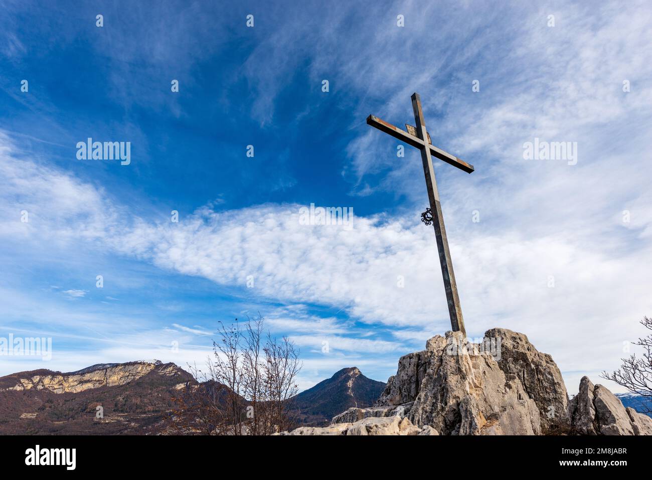 Religiöses Metallkreuz auf einem Berggipfel (Monte Altissimo di Nago) vor einem blauen Himmel mit Wolken und Kopierraum. Trentino Alto Adige, Italien, Europa. Stockfoto
