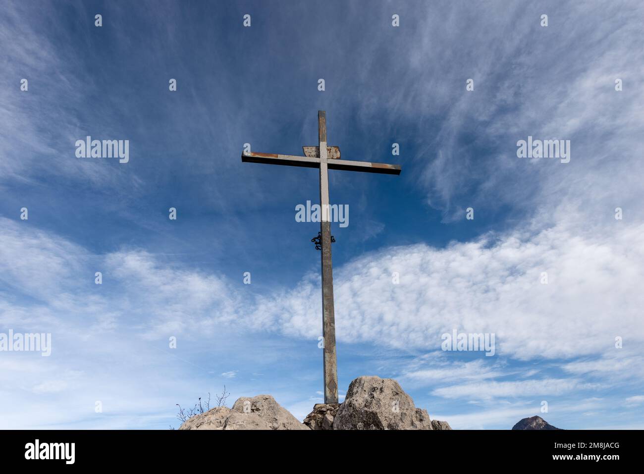 Religiöses Metallkreuz auf einem Berggipfel (Monte Altissimo di Nago) vor einem blauen Himmel mit Wolken und Kopierraum. Trentino Alto Adige, Italien, Europa. Stockfoto
