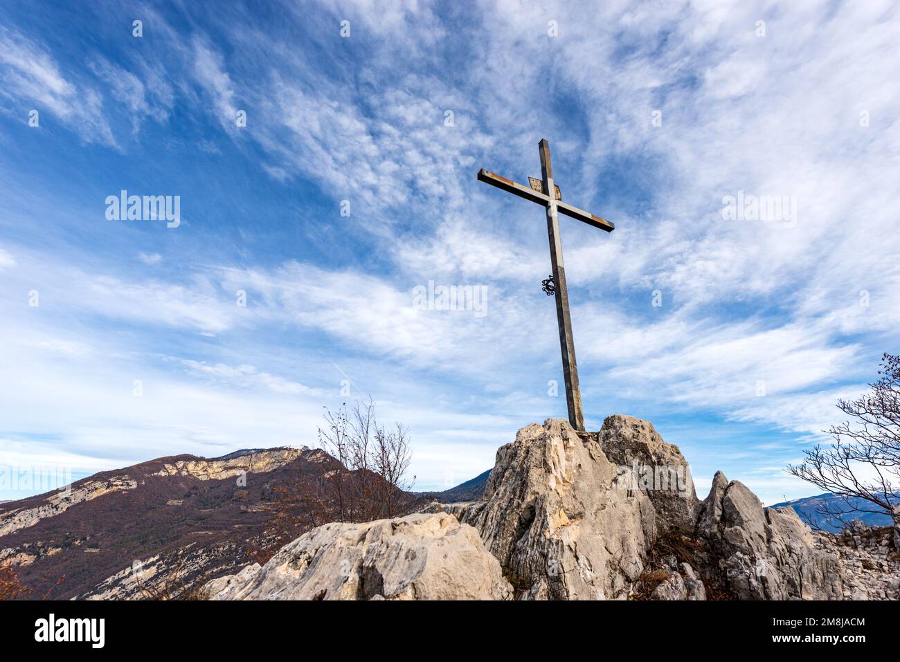 Religiöses Metallkreuz auf einem Berggipfel (Monte Altissimo di Nago) vor einem blauen Himmel mit Wolken und Kopierraum. Trentino Alto Adige, Italien, Europa. Stockfoto