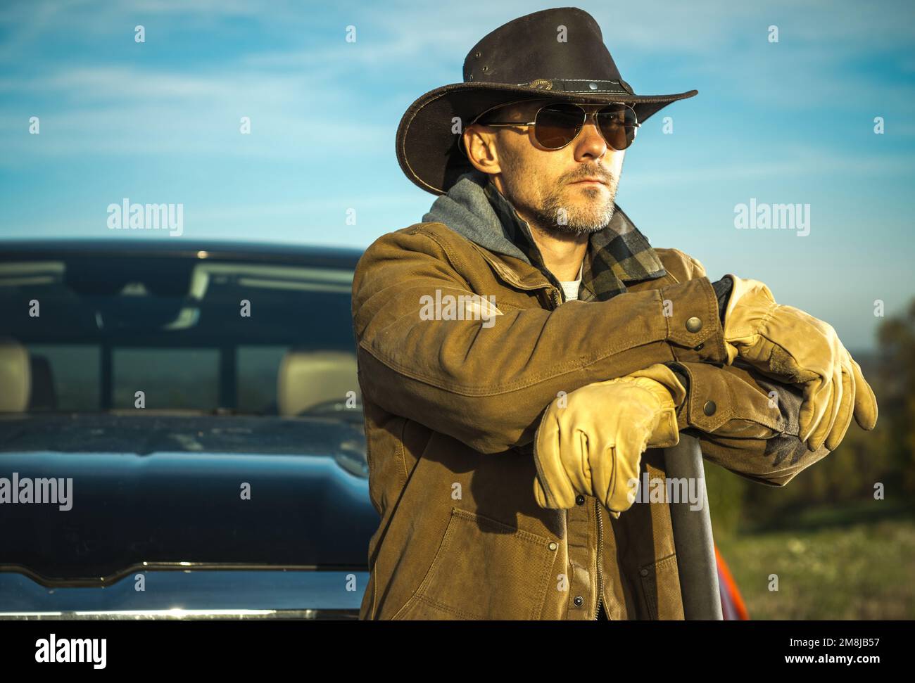 Caucasian Rancher trägt Cowboyhut und Sonnenbrille und bleibt vor seinem Pickup Truck. Amerikanisches Bauernmotiv. Stockfoto