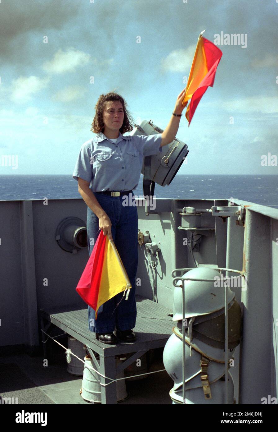 An Bord des U-Boot-Tenderschiffs USS HOLLAND (AS-32) demonstriert Signalman SEEMANN APPRENTICE (SNSA) Carey Gross mehrere Flaggensignale, die für die Kommunikation mit anderen Schiffen auf See verwendet werden. Land: Pazifik (POC) Stockfoto