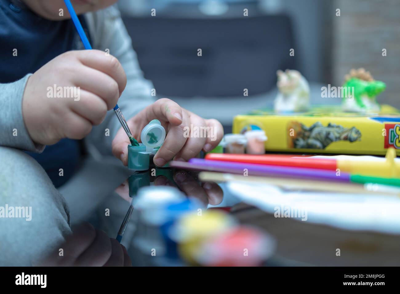 Nahaufnahme eines Jungen, der einen Pinsel in eine Flasche Farbe tauchte. Im verschwommenen Hintergrund sehen Sie die Figuren, die der Junge färbt Stockfoto