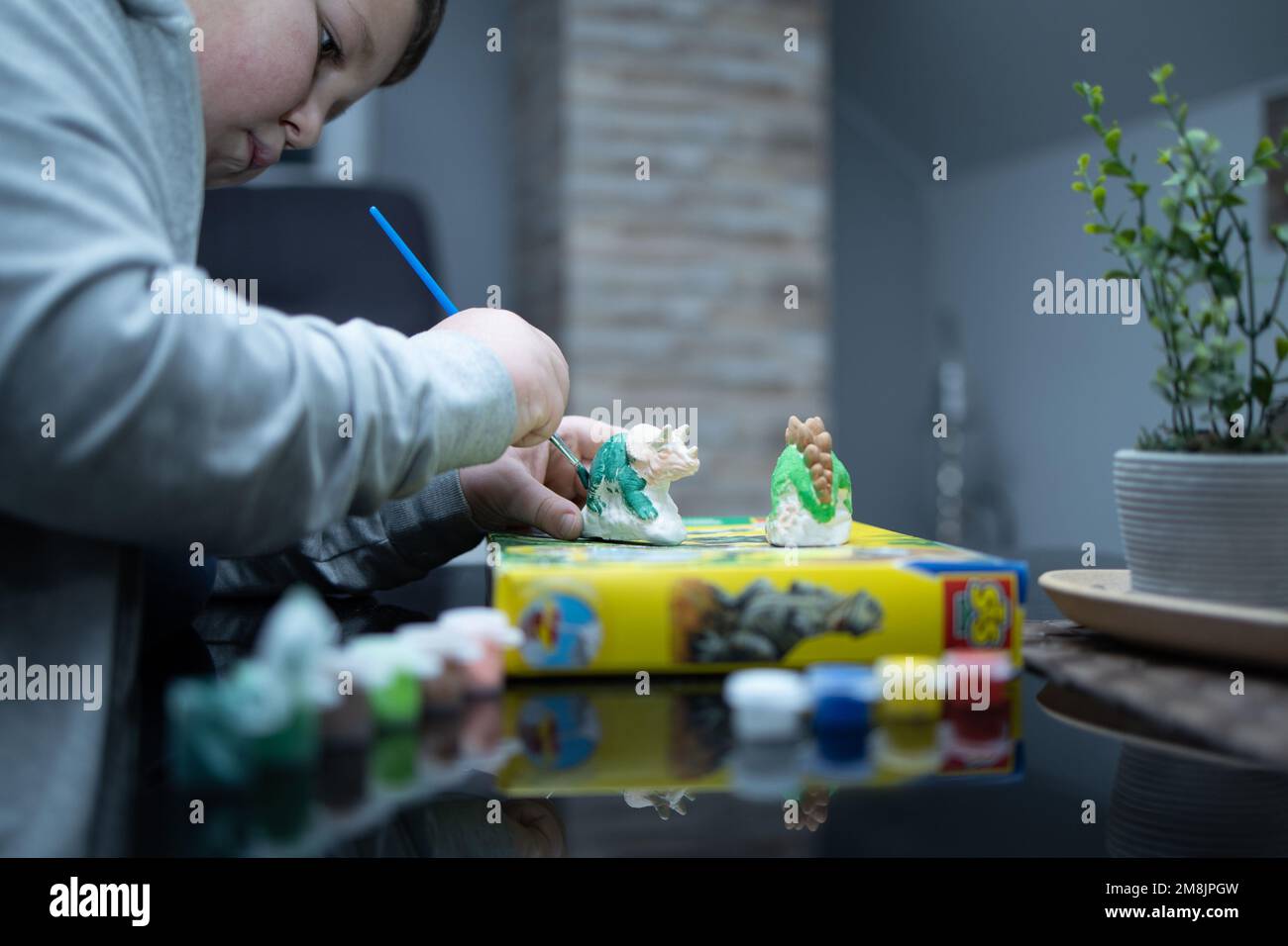 Ein Junge färbt eine Dinosaurierfigur. Nahaufnahme. Im Fokus steht der Pinsel, mit dem der Junge Farbe auf die Figur aufträgt Stockfoto