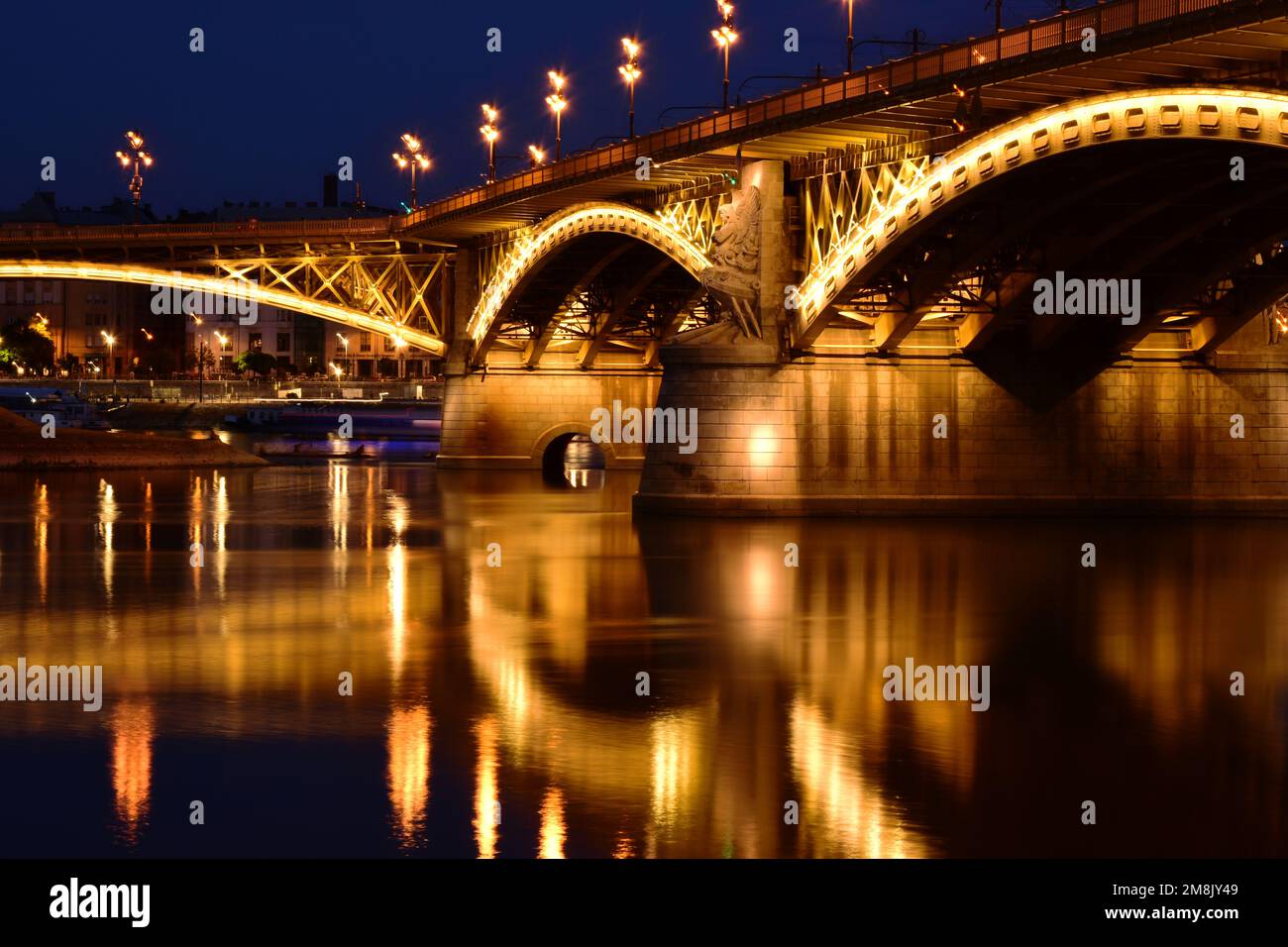 Die Margaretenbrücke in Budapest in der Dämmerung. Perspektivische Seitenansicht. Hell beleuchtete Stahlbögen. Reflexion über das Wasser. Tourismus und Reisekonzept Stockfoto