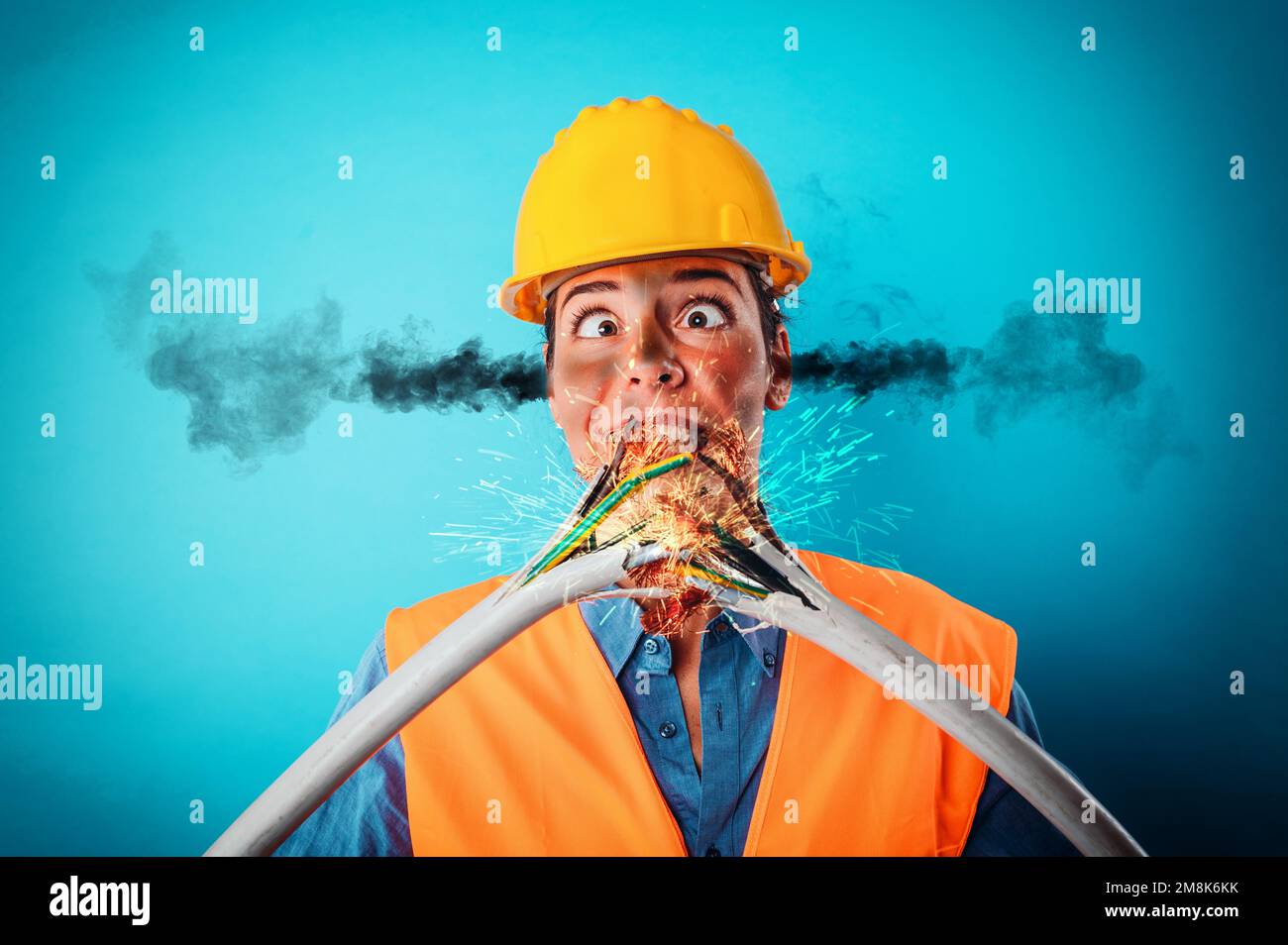 Ein schockiertes Arbeitermädchen mit Helm zerbricht ein Stromkabel Stockfoto