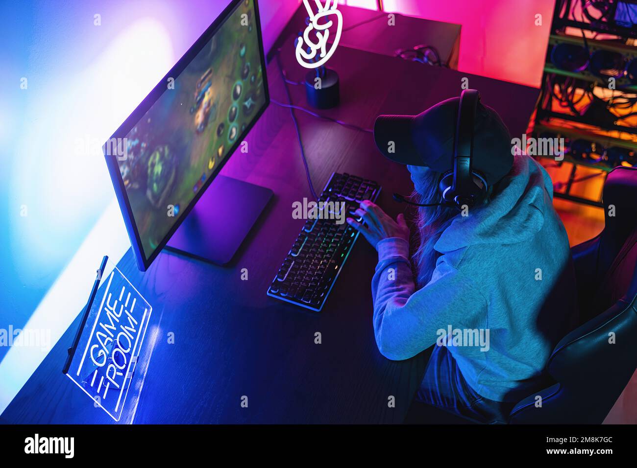 Professionelle Gamer, die Ego-Shooter Online-Videospiel auf ihrem leistungsstarken PC spielt. Zimmer und PC verfügen über farbenfrohe Neon-LED-Lichter. Stockfoto