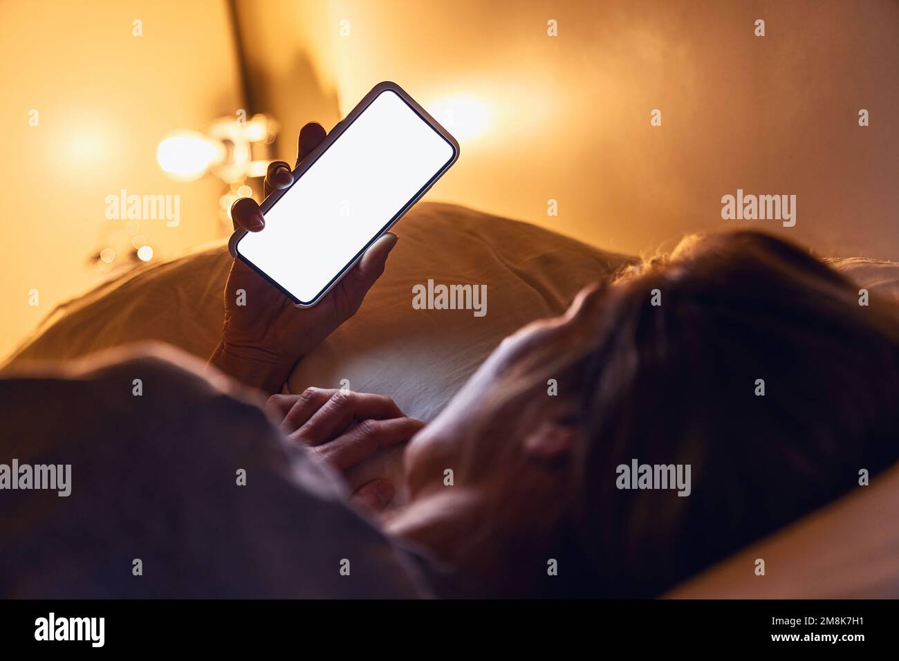 Frau, die ihr Smartphone spät nachts in der Hand hält, mit weißem Hintergrund für Kopierraum im Bett. Person, die in einem dunklen Zuhause auf eine leere Telefon-App schaut. Sexting oder Stalking Stockfoto