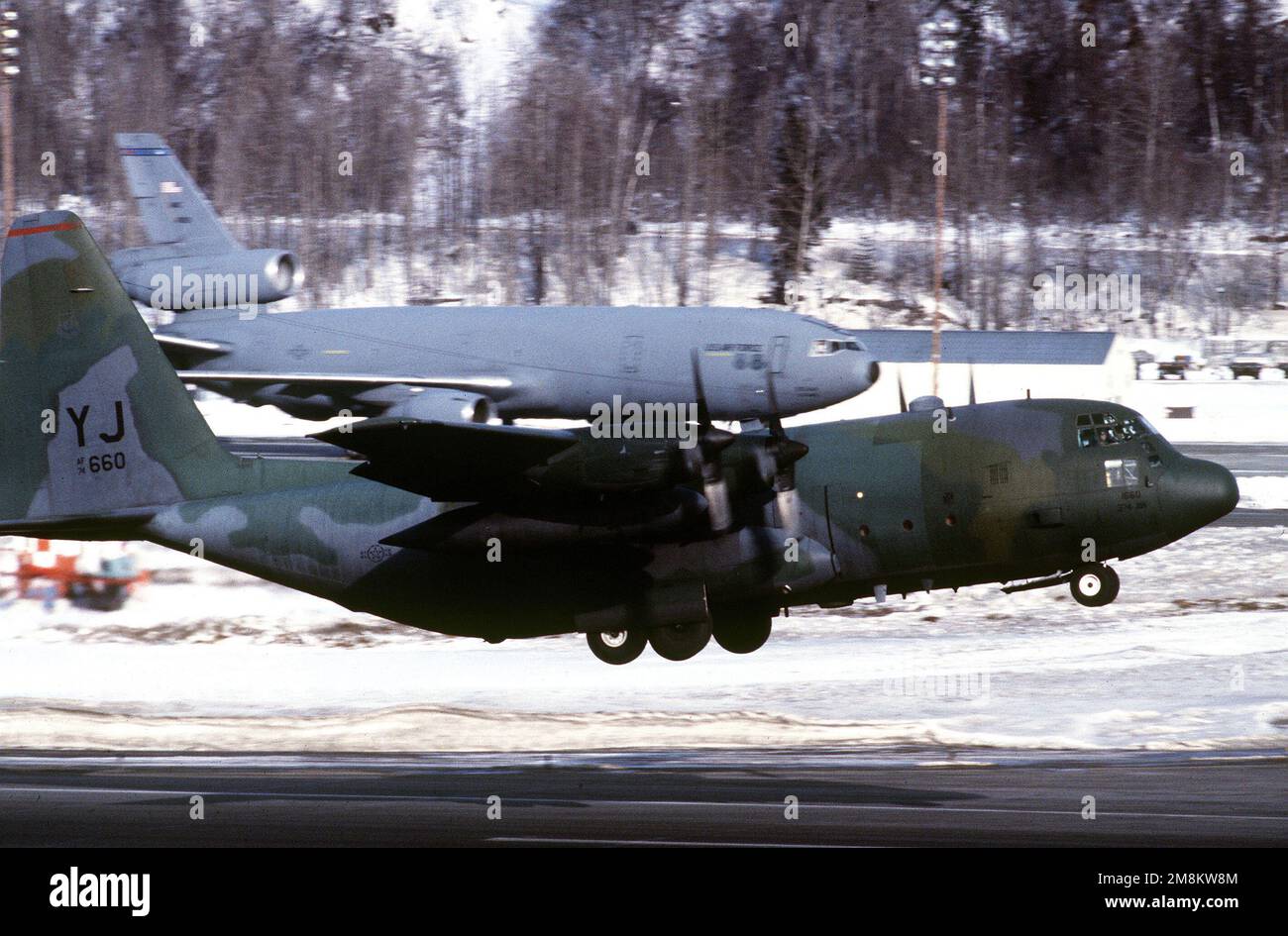 C-130 von der 36. Airlift-Geschwader, Yokota Japan startet von der schneefreiliegenden Landebahn 05. Im Hintergrund befindet sich ein Transient Air Mobility Command (AMC) KC-10-Tankschiff. Basis: Luftwaffenstützpunkt Elmendorf Bundesstaat: Alaska (AK) Land: Vereinigte Staaten von Amerika (USA) Stockfoto