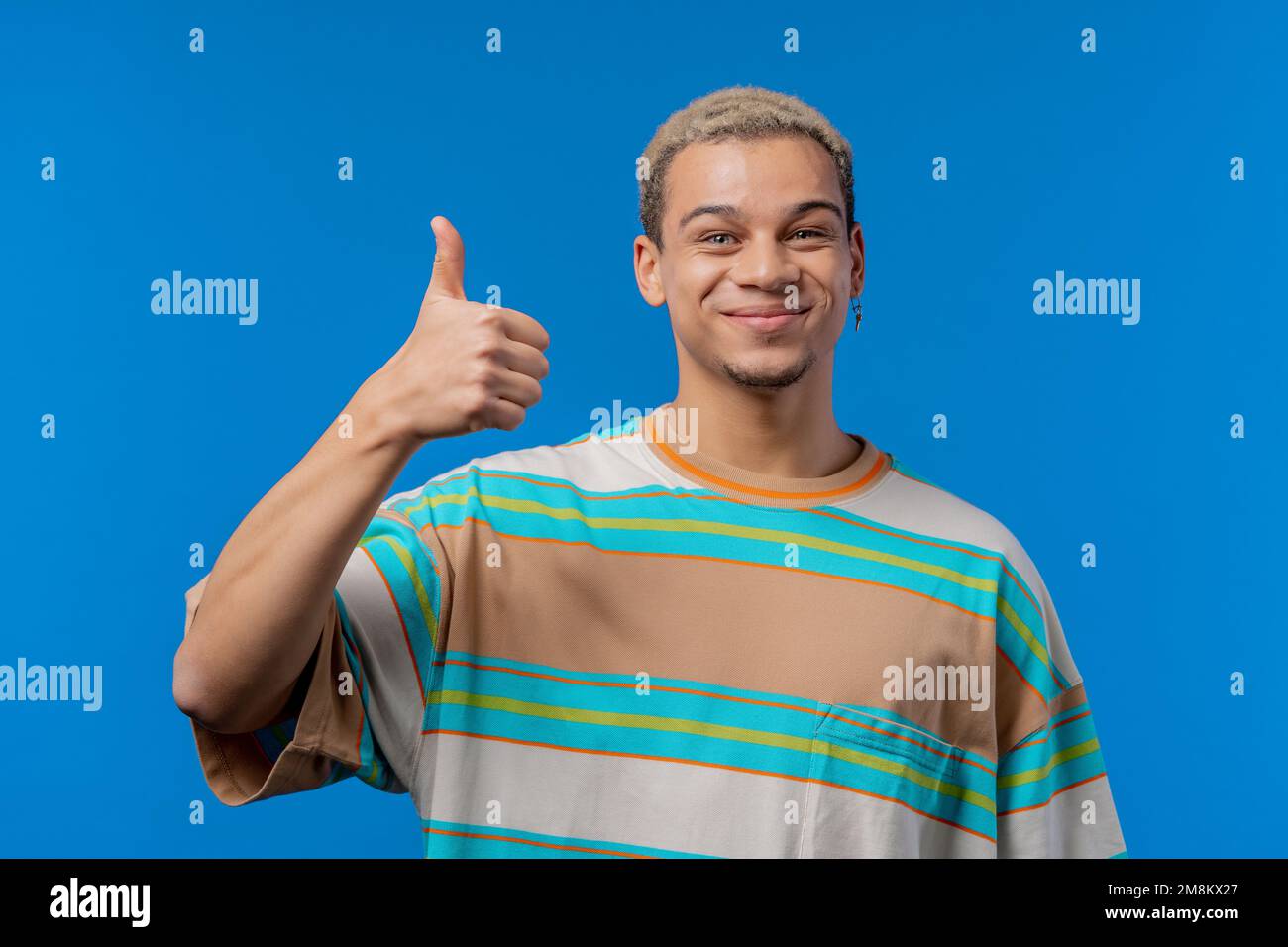 Ein positiver Mann macht Handzeichen wie eine Daumen-hoch-Geste. Glücklicher Schüler in Blau, richtige perfekte Wahl, tolles Angebot, Studiohintergrund. Stockfoto