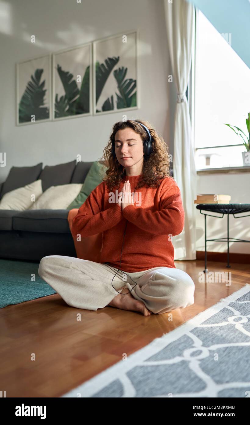 Eine junge, aufmerksame Frau mit Kopfhörern, die zu Hause meditiert. Vertikal Stockfoto