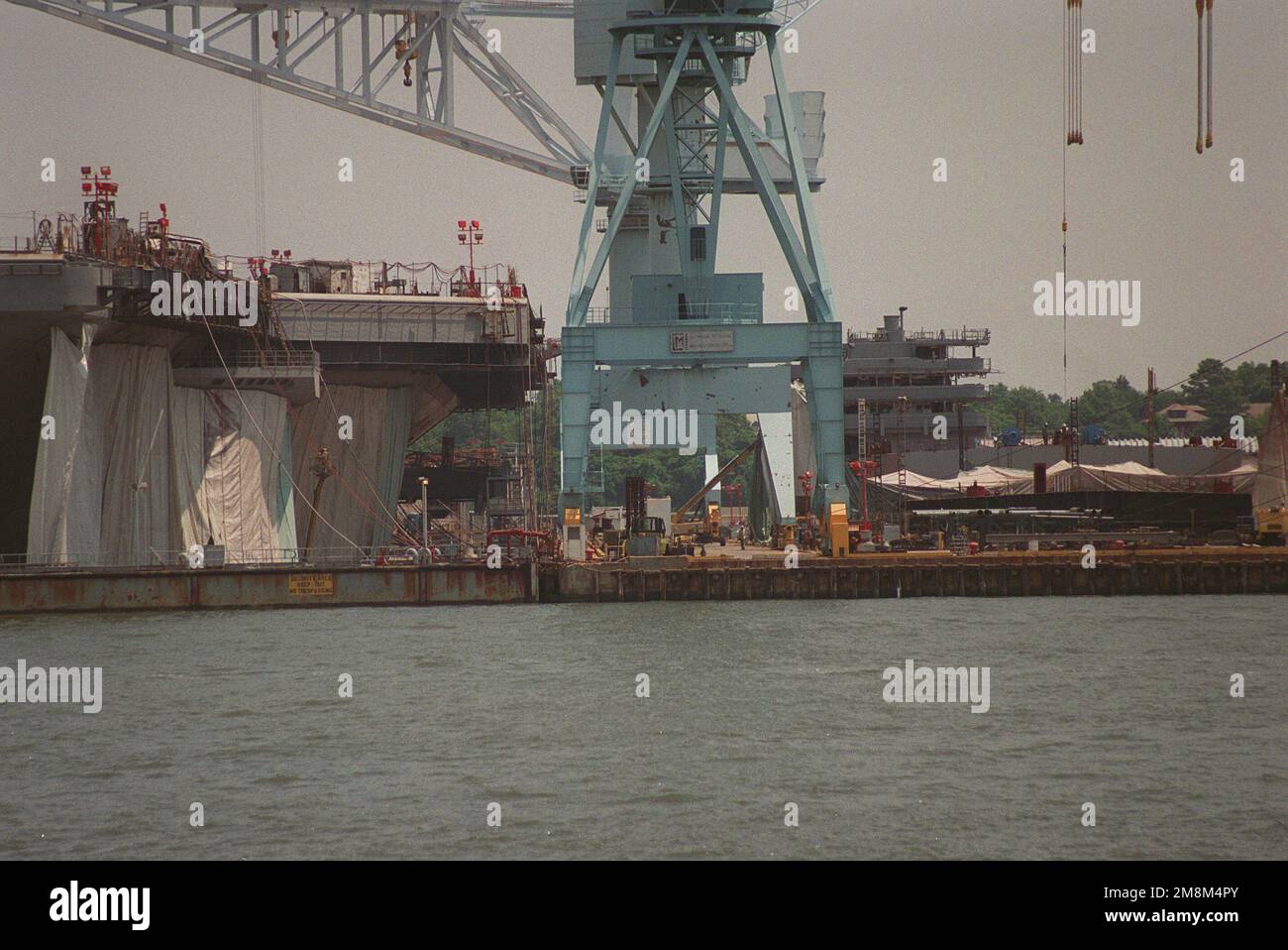 Nahaufnahme des nuklearbetriebenen Flugzeugträgers HARRY S. TRUMAN (CVN-75), der im Trockendock Nr. 12 am Newport News Shipbuilding und der Drydock Corporation Shipyard gebaut wird. DER TRUMAN-Rumpf befindet sich links vom Kran, die Inselstruktur des Schiffs ist rechts vom Kran in modularer Bauweise zu sehen und wird am 11. Juli fertiggestellt an Bord gebracht. Basis: James River Bundesstaat: Virginia (VA) Land: Vereinigte Staaten von Amerika (USA) Stockfoto