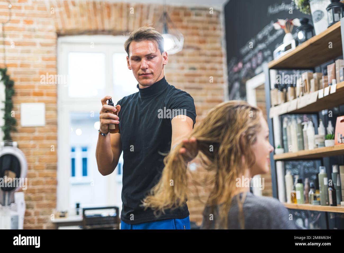 Friseur-Mann, der Spray auf die nassen Haare des Klienten benutzt, Haarpflegekonzept Medium Shot. Hochwertiges Foto Stockfoto