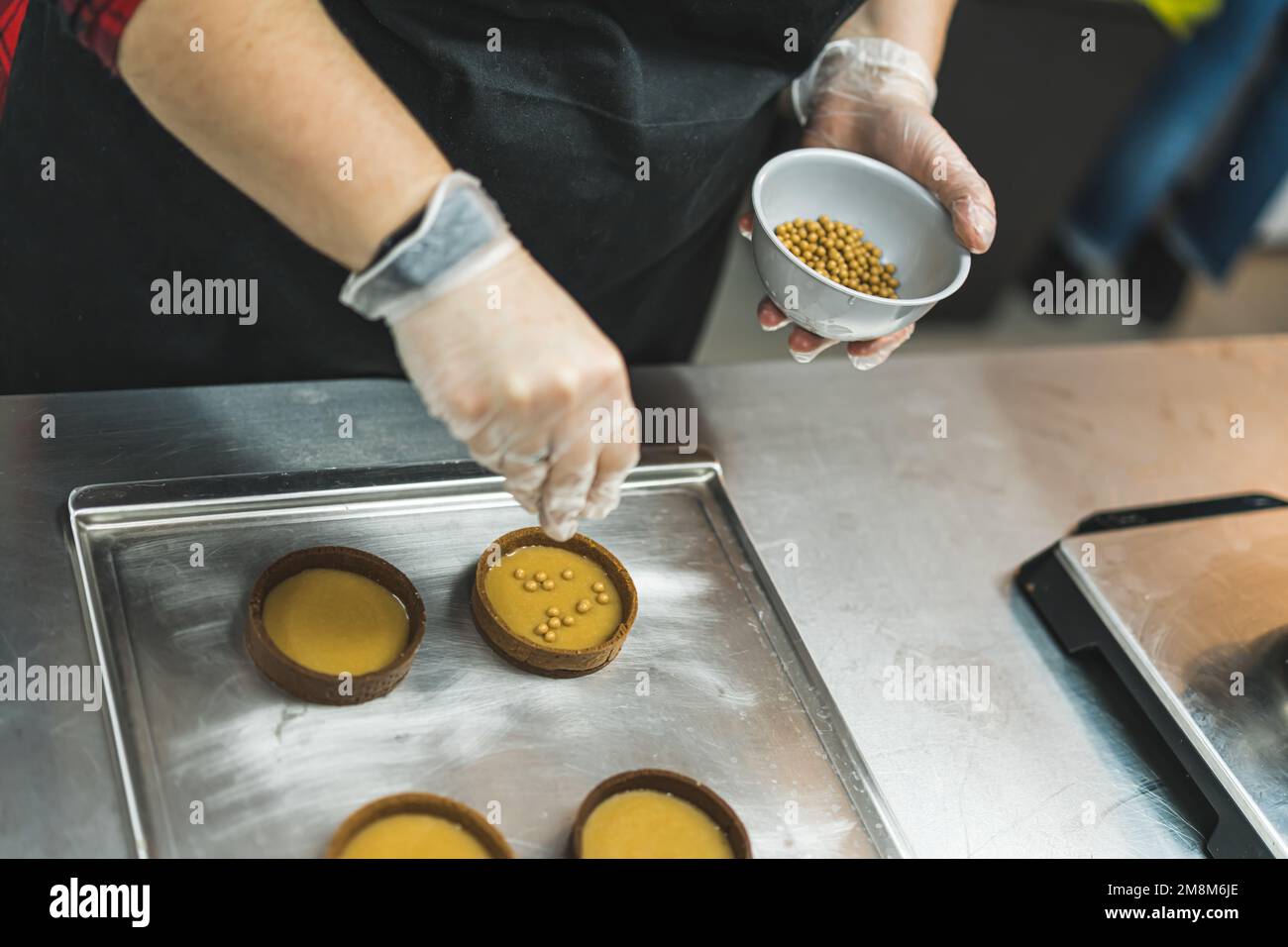 Blick von oben auf die Hände des Küchenchefs mit goldenen Streuseln zu runden Kuchen in der Bäckerei. Hochwertiges Foto Stockfoto