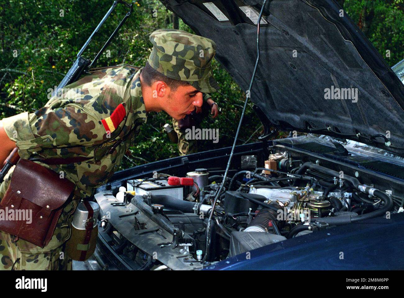 Ein rumänischer Soldat sucht unter der Motorhaube eines Fahrzeugs, das während der Situationstraining-Übung 5 (STX-5), Teil der Operation OSPREY '96, versucht, seine Straßensperre in Camp Lejeune, NC, zu passieren. Ein rumänischer Soldat sucht unter der Motorhaube eines Fahrzeugs, das während der Situationstraining-Übung 5 (STX-5), Teil der Operation OSPREY '96, versucht, seine Straßensperre in Camp Lejeune, NC, zu passieren. Stockfoto