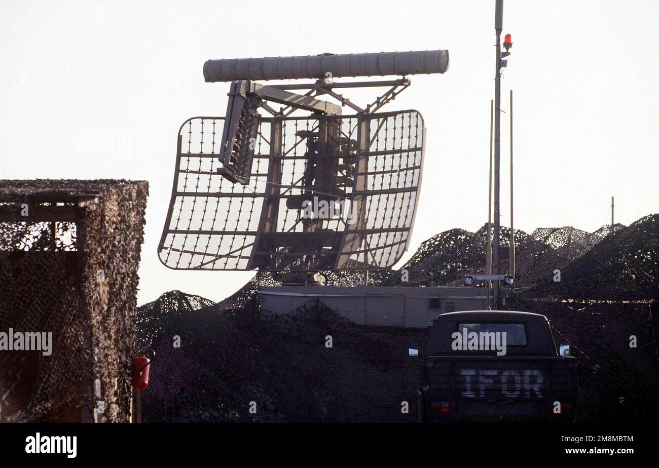 EINE AN/TPN-24-ARS-Antenne (Airfield Surveillance Radar), Teil des AN/TPN-19 Landing Control Central Transportable Surveillance Radar Systems, das mit Tarnnnetzen abgedeckt ist und im Radar Approach Control Center am Luftwaffenstützpunkt Tuzla, Bosnien-Herzegowina, verwendet wird. Ein IFOR-markiertes Fahrzeug wird im Vordergrund geparkt. Basis: Tuzla Air Base Country: Bosnien und Herzegowina (BIH) Stockfoto