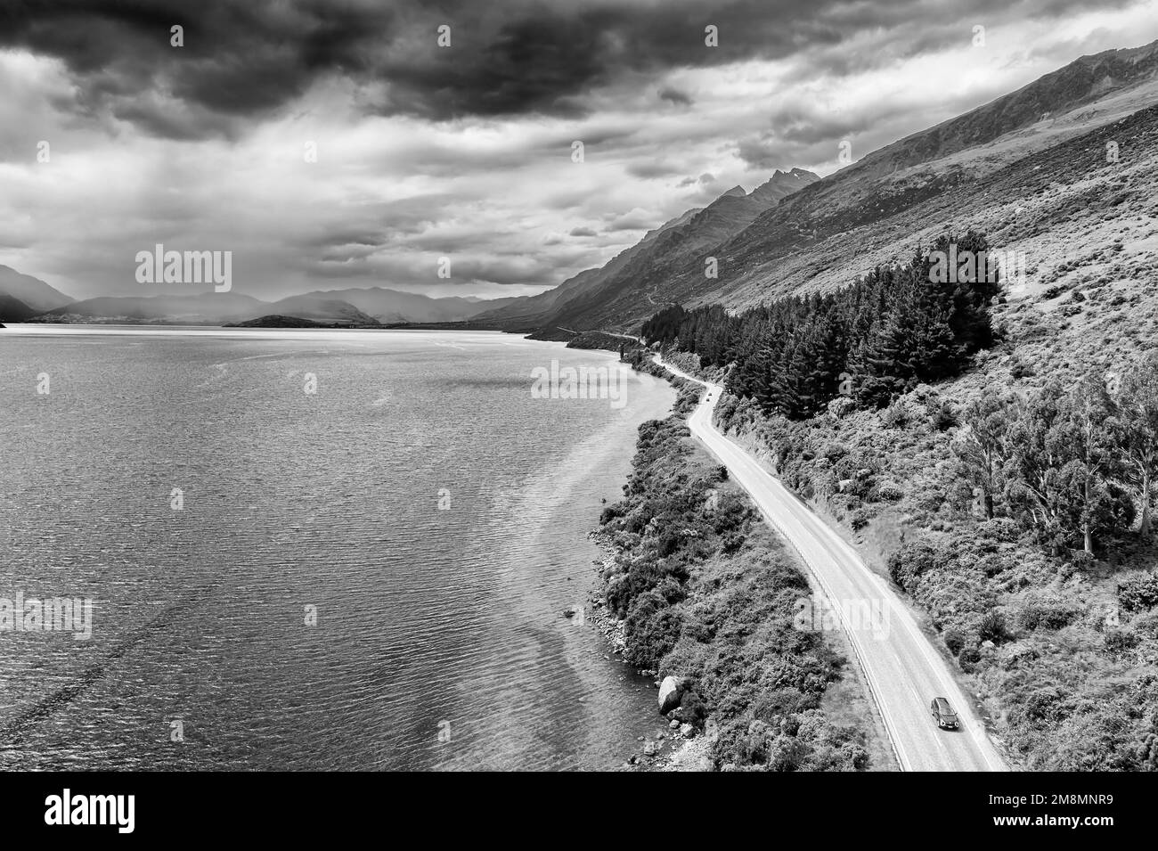Dramatischer, kontrastreicher schwarzweißer Blick auf das Auto auf dem Highway 6 entlang des Lake Wkatipu in Otago von Neuseeland - malerische Luftlandschaft. Stockfoto