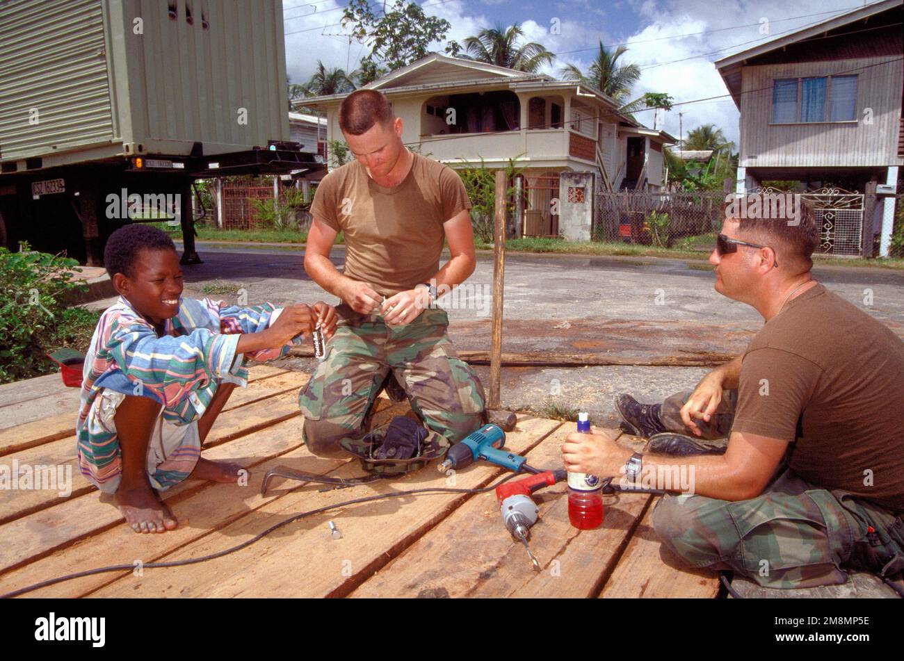 Guyanesischer Teenager, Andrea, Corporal Daniel J. Warren und SGT. Paul A Dresher, von der Marine Support Squadron 274, Cherry Hill, N.C., machen Sie eine Pause vom Brückenbau vor Onkel Eddies Altersheim. Das Seniorenheim in Georgetown wird während der ersten kombinierten humanitären und bürgerschaftlichen Hilfsaktion, die 97 zwischen den Vereinigten Staaten und Guyana durchgeführt wurde, renoviert. Militärpersonal der Luftwaffe, der Luftwaffenreserve und der Nationalgarde, der Armee, der Nationalgarde der Armee und des Marine Corps nahmen an der Übung Teil, die eine technische und medizinische Bereitschaftsausbildung umfasste. Stockfoto