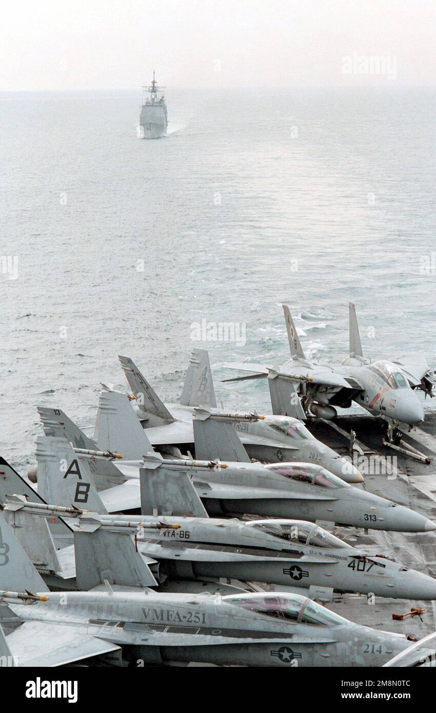 Aus Sicht des Cockpits des nukleargetriebenen Flugzeugträgers USS GEORGE WASHINGTON (CVN 73) nähert sich der geführte Raketenkreuzer (AEGIS) USS NORMANDY (CG 60) während der Vorbereitungen für die laufende Wiederauffüllung von hinten. US Marine Corps F/A-18C Hornets, US Navy F/A-18C und eine F-14B Tomcat sind auf dem Flugdeck im Vordergrund geparkt. Beide Schiffe führen derzeit Operationen im Persischen Golf durch, um UN-Sanktionen gegen Irak durchzusetzen. Operation SÜDWACHE, 21. Februar 1998. Betreff Betrieb/Serie: SÜDLICHE WACHSTATION: USS George Washington (CVN 73) Stockfoto