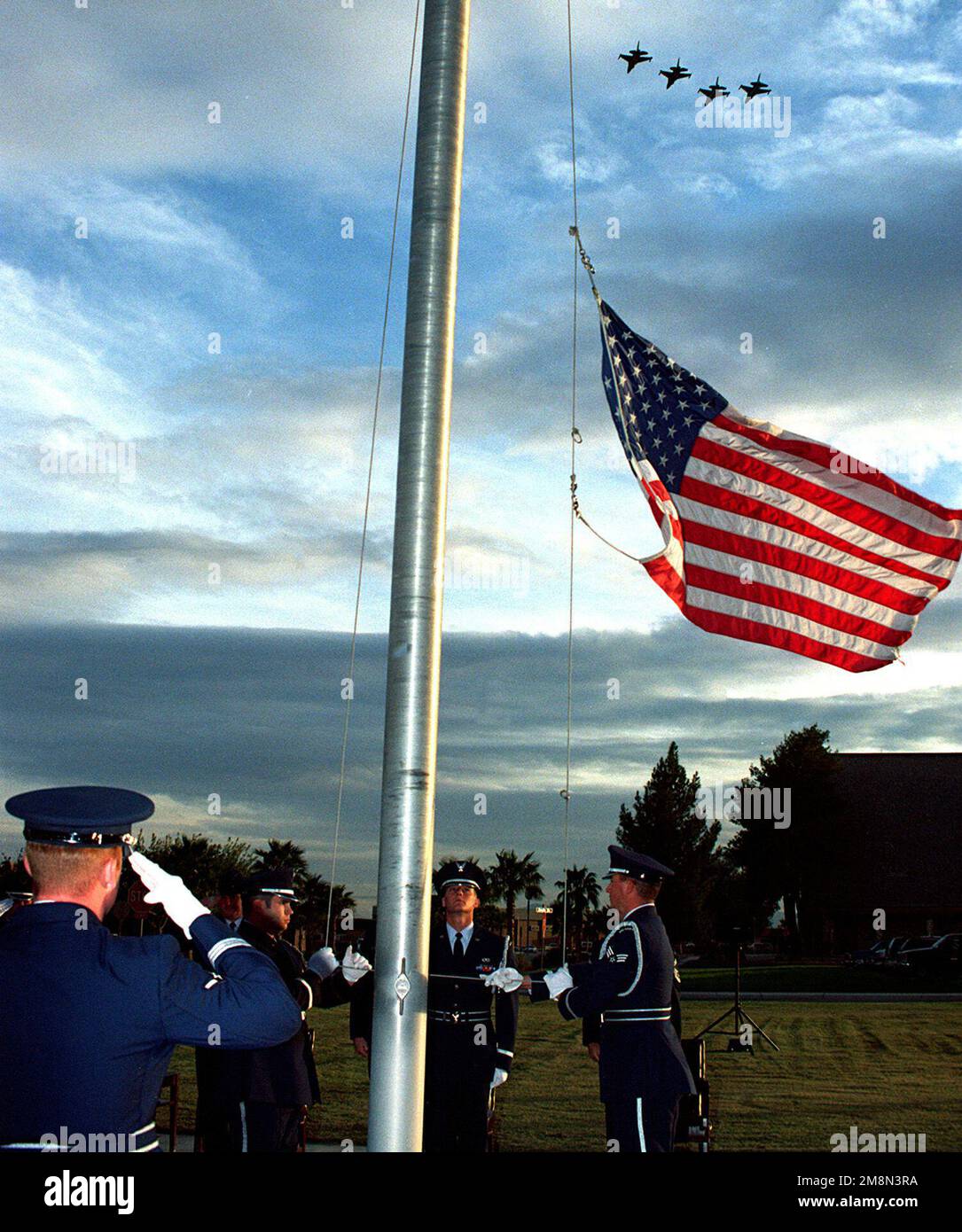 Mitglieder der Nellis AFB Ehrengarde senken die US-Flagge bei einer Ruhestand-/Rückzugszeremonie, während ein vier-Schiff F-16s vorbeifliegt. Das Team ist der zweitbeste der Air Force Honor Guard auf dem Arlington National Cemetery, da es in einem Jahr Details aufführt. Basis: Luftwaffenstützpunkt Nellis Bundesstaat: Nevada (NV) Land: Vereinigte Staaten von Amerika (USA) Stockfoto