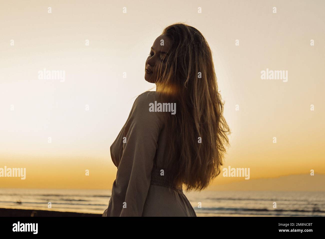Ein wunderschönes Mädchen in einem Kleid und Schmuck im Hintergrund des Sonnenuntergangs im Hintergrund des Meeres, eine Frau mit langen Haaren im Urlaubsporträt Stockfoto