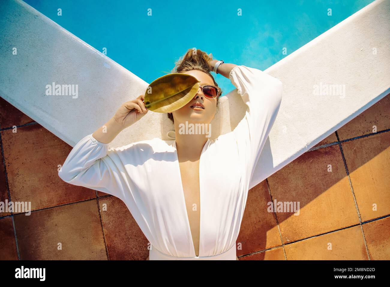 Modefoto eines Models am Außenpool, Bäume, tropischer Stil. Weißer Badeanzug einer Frau mit langen Haaren. Sommerferien, Reisen Stockfoto