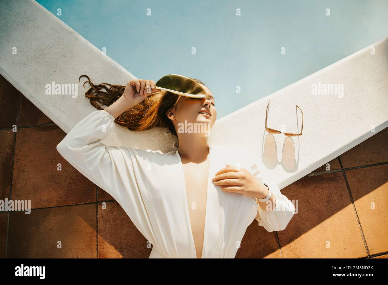 Modefoto eines Models am Außenpool, Bäume, tropischer Stil. Weißer Badeanzug einer Frau mit langen Haaren. Sommerferien, Reisen Stockfoto