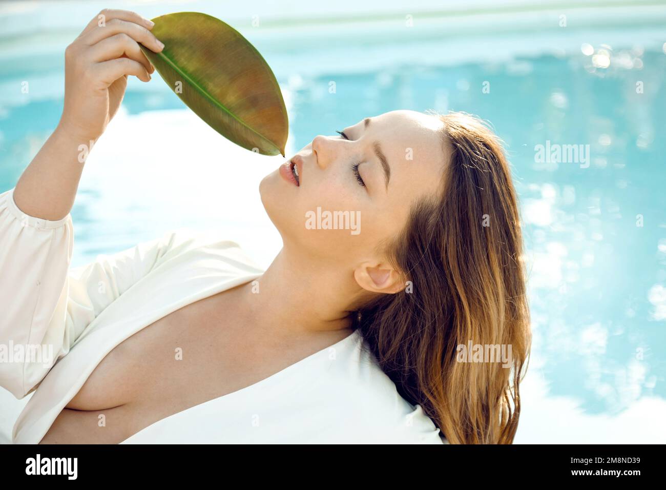 Ein modisches Mädchen in einem stilvollen weißen Badeanzug liegt draußen am Pool. Schöne Frau, die sich auf Reisen, im Spa und im Laub ausruht Stockfoto