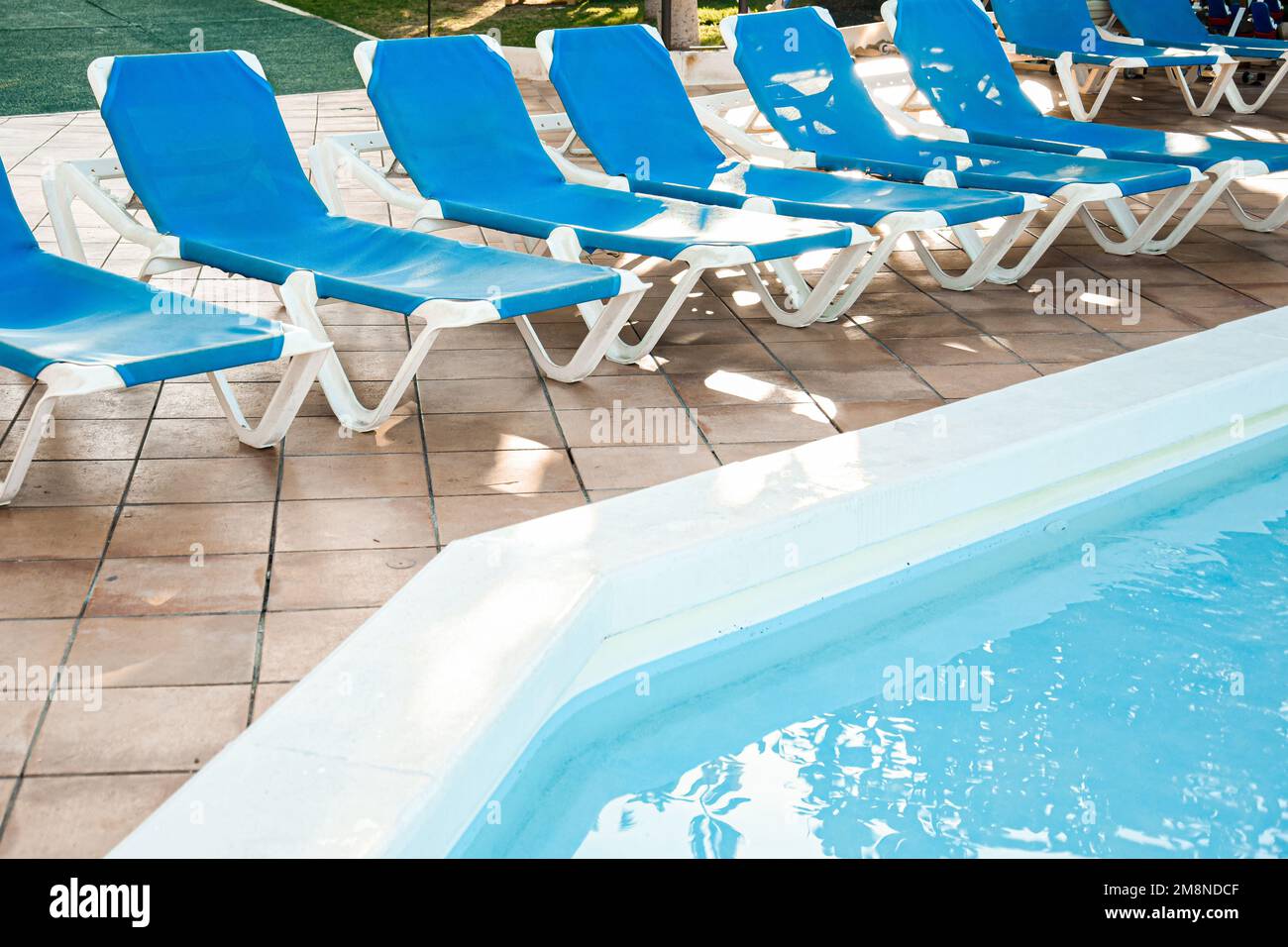 Foto des Swimmingpools von oben auf der Straße und blaue Sonnenliegen in der Nähe. Sommer und Ruhe Stockfoto
