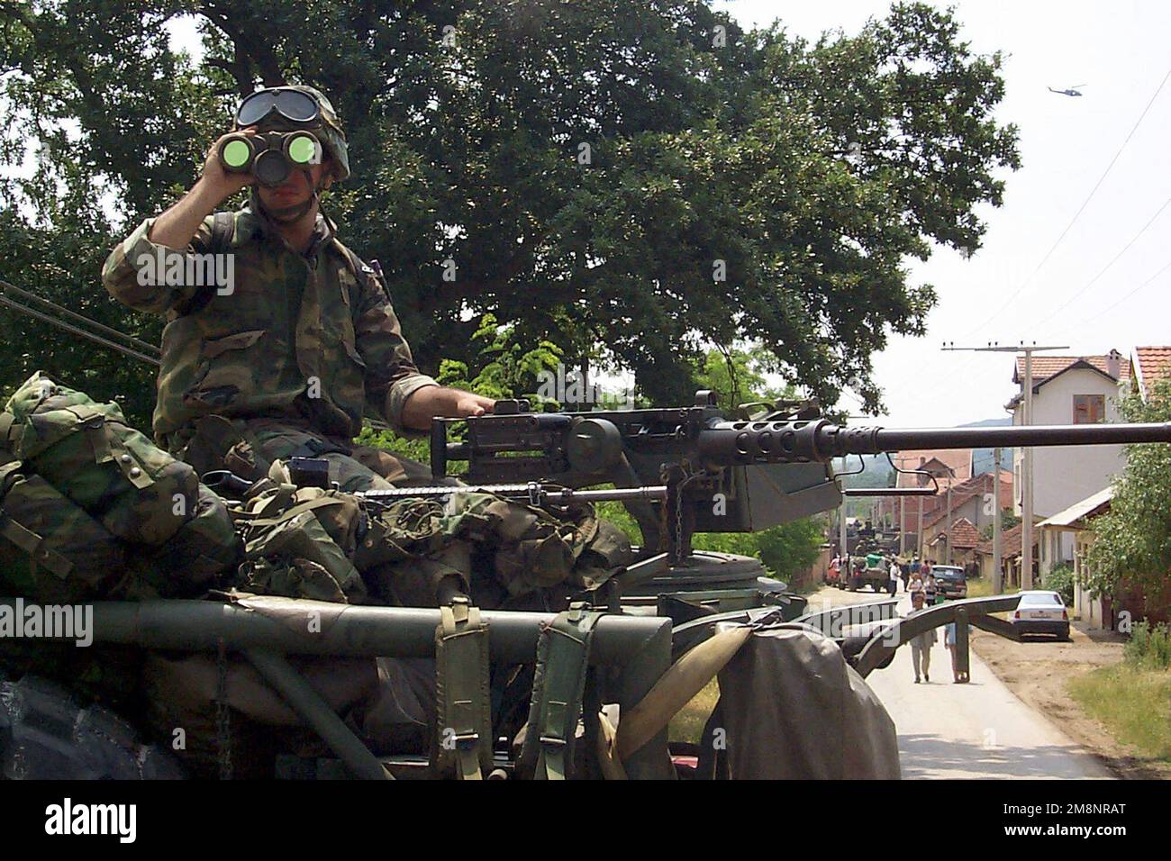 EIN US-AMERIKANISCHER Ein Maschinenschütze der 26. Marine Expeditionary Unit (MEU), 3. Bataillon, 8. Marines, der ein schweres Maschinengewehr des Kalibers Browning m2 HB 0,50 besetzt, blickt durch ein Fernglas, während er die Straße einer kleinen Stadt in der Nähe des vorderen Operationsstützpunktes scannt, während einer Parade von Soldaten der Kosovo Liberation Army. Elemente der 26. MEU, die von Schiffen der Amphibienbereitschaft-Gruppe 2 (nicht abgebildet) zur Unterstützung der NATO-Operation Joint Guardian eingesetzt wurden. Betrifft Operation/Serie: GEMEINSAMER VORMUNDSTAAT: Kosovo-Land: Jugoslawien (YUG) Stockfoto