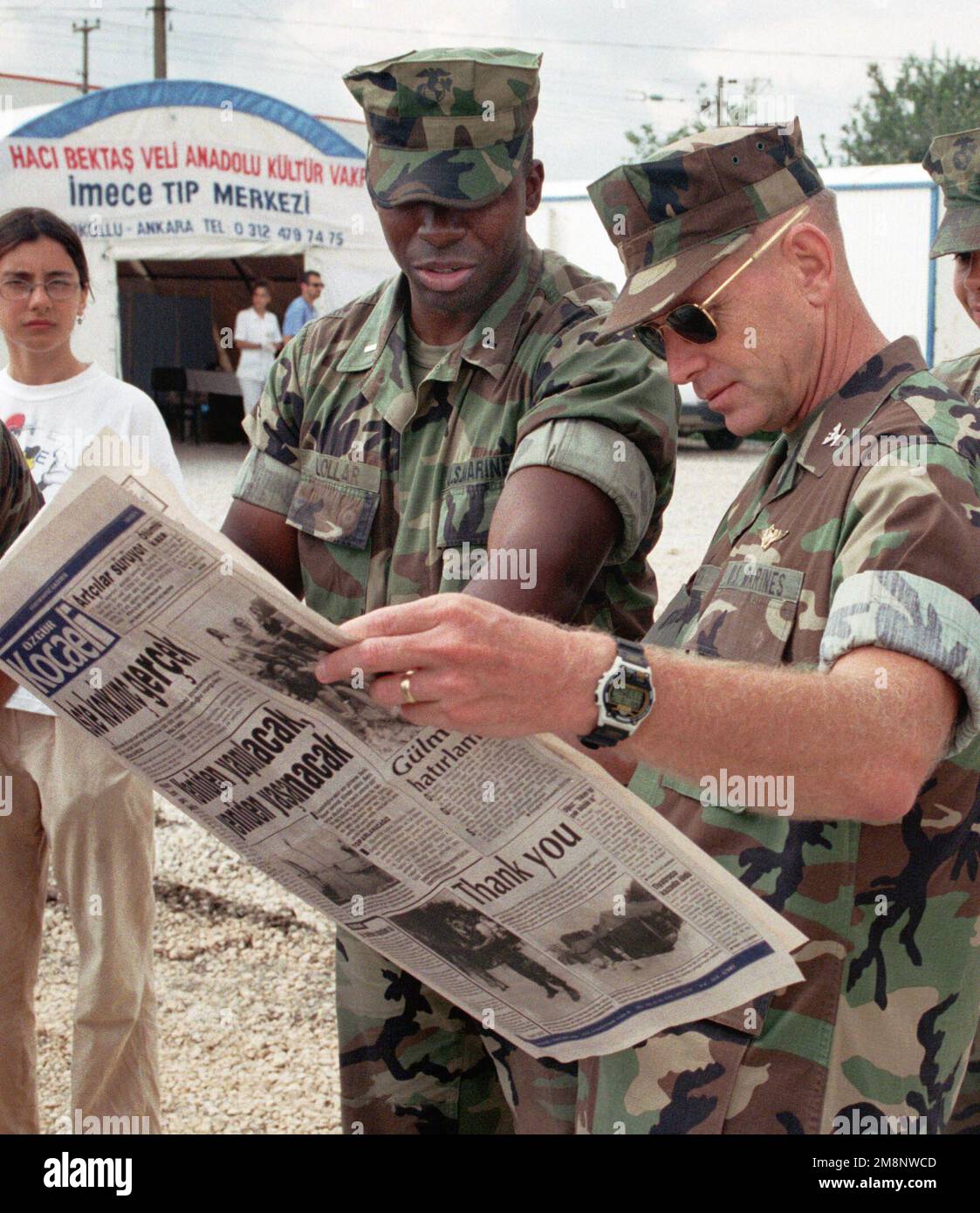 Während der Operation AVID RESPONSE (OAR) zeigt der erste Lieutenant Charles Lollar (links) Fotos in einer türkischen Zeitung von Marines, die Zelte aufstellen, an Colonel Kenneth J. Glueck, den kommandierenden Offizier der 26. Marineexpeditionstruppe (SONDEREINSÄTZE MÖGLICH). (MEU(SOC)) während sie im Roten Halbmond-Lager in Dogu Kisla, Türkei, auf die Ankunft von Außenministerin Madelaine Albright warten. OAR ist der Beitrag des US-Kommandos Europa zur Unterstützung der Hilfsmaßnahmen nach dem Erdbeben, das etwa 65 Meilen östlich von Istanbul in der Nähe der Stadt Izmit wütete. Türkische Beamte schätzen auf etwa 600 Stockfoto