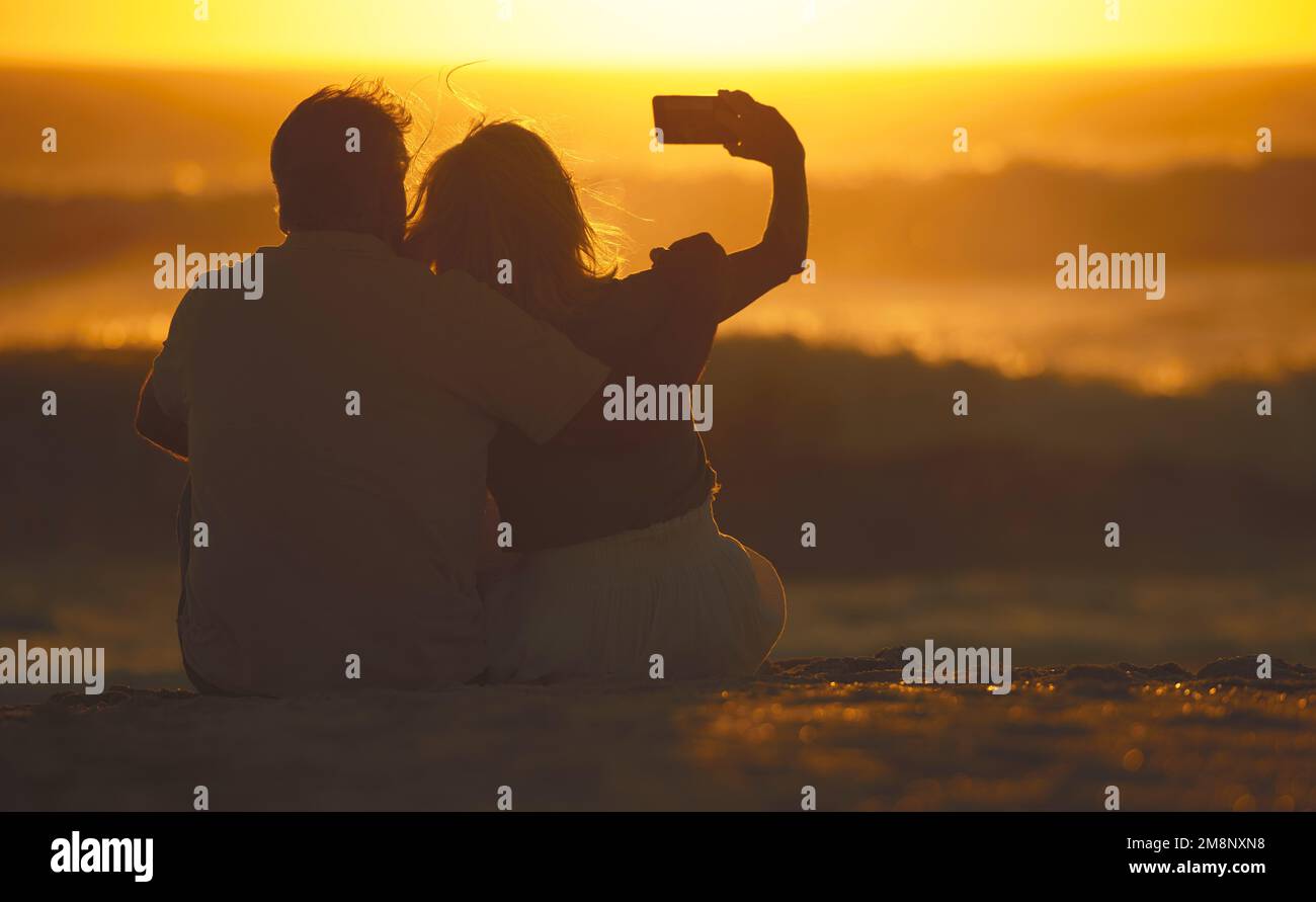 Ein älteres Paar, das Selfies am Strand macht. Reife Frau, die ein Handy benutzt, um Fotos am Strand zu machen. Sorgenfreies, reifes Paar, das Fotos macht Stockfoto