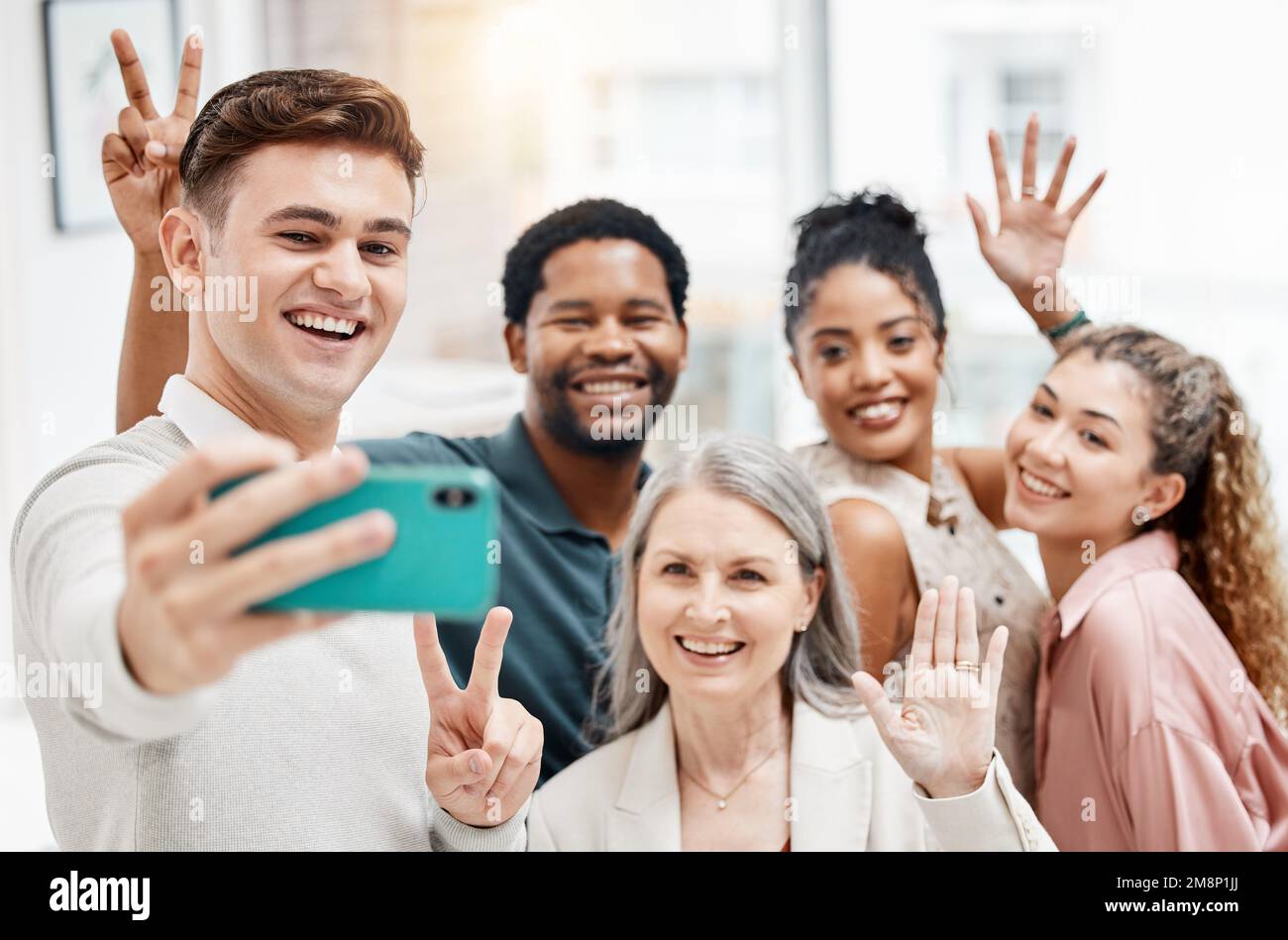 Eine Gruppe fröhlicher und vielseitiger Geschäftsleute, die gemeinsam ein Selfie bei der Arbeit machen. Glücklicher weißer Geschäftsmann, der ein Foto mit seinen Kollegen macht Stockfoto