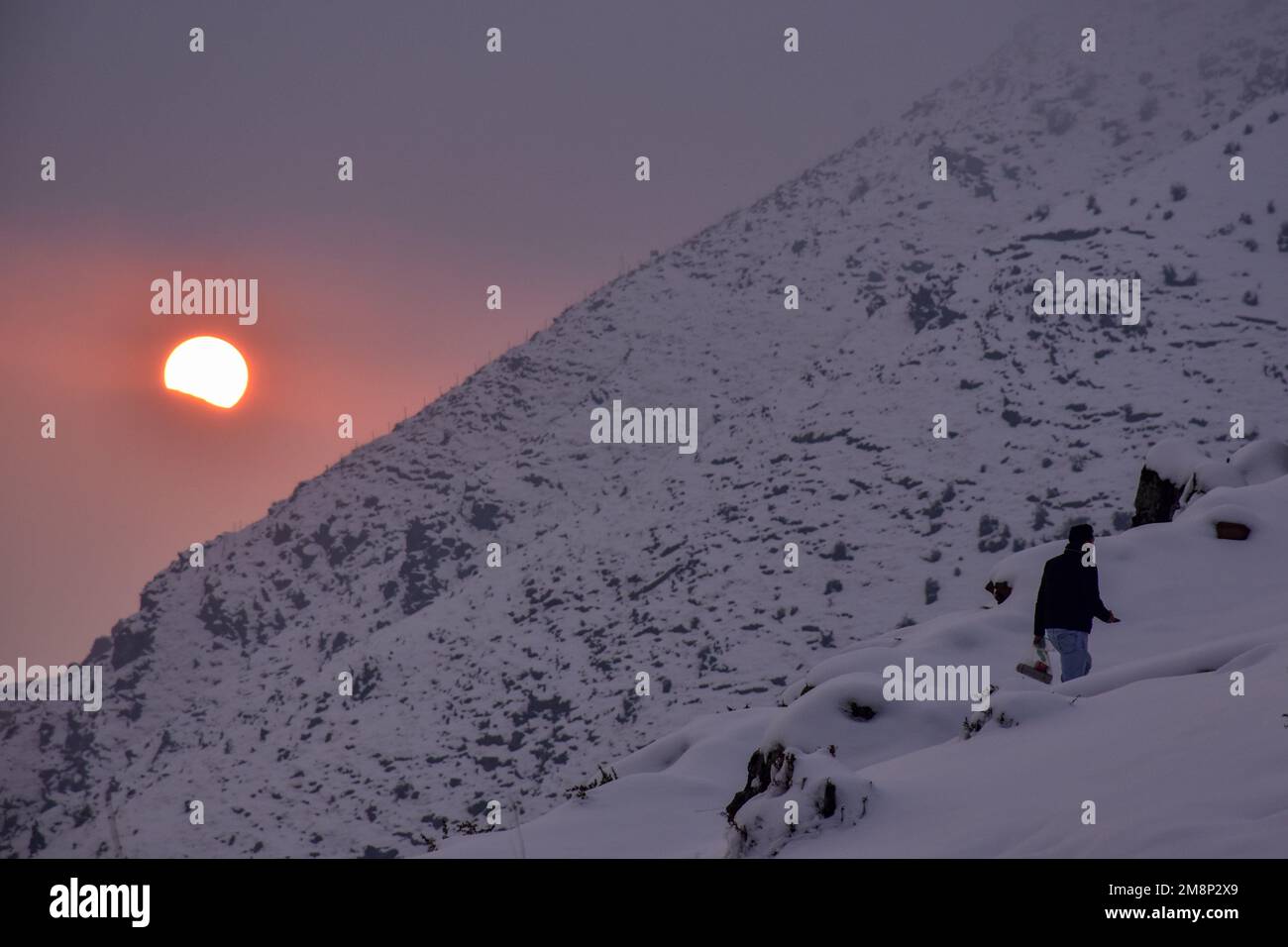 Srinagar, Indien. 14. Januar 2023. Ein Mann geht den schneebedeckten Hügel entlang während des Sonnenuntergangs am Stadtrand von Srinagar. Das Wetter verbesserte sich im Kaschmir-Tal nach Tagen mit moderatem bis starkem Schneefall und Regen. In der Zwischenzeit wurden am Samstag Lawinen im Bezirk Bandipora und im Bahnhof Sonamarg gemeldet, bei denen es in den letzten Tagen zu moderaten bis schweren Schneefällen kam. Dies ist der zweite Vorfall, der in den letzten zwei Tagen in der beliebten Hill Station gemeldet wurde. Zwei Arbeiter starben am Donnerstag, als eine Lawine die Baustelle einer Baufirma in Sonamarg traf. Kredit: SOPA Images Limited/Alamy Stockfoto