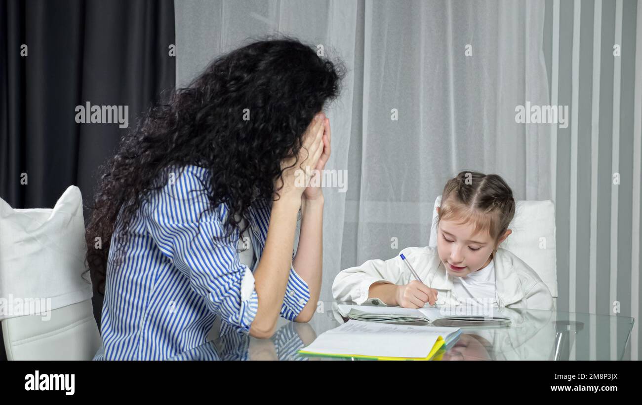 Erschöpfte Mutter prüft Hausaufgaben der Tochter und sieht müde aus Stockfoto