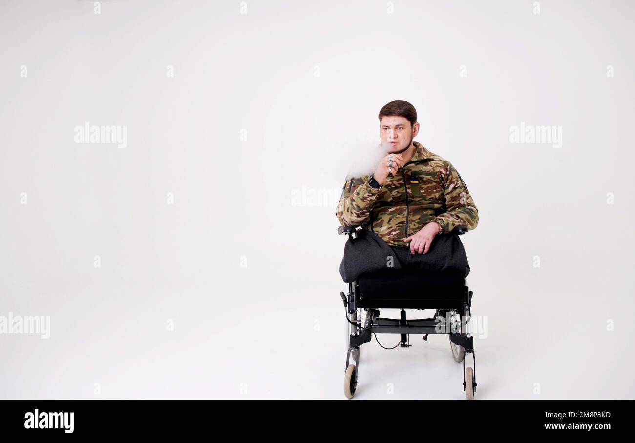 Militärmann in Uniform sitzt und raucht Er atmet Rauchpuppen aus Er hat Ringe an seinen Fingern Emblem der Ukraine die ukrainische Flagge ist auf Schutzjacke genäht Erwachsener attraktiver Mann 35 Jahre alt Stockfoto