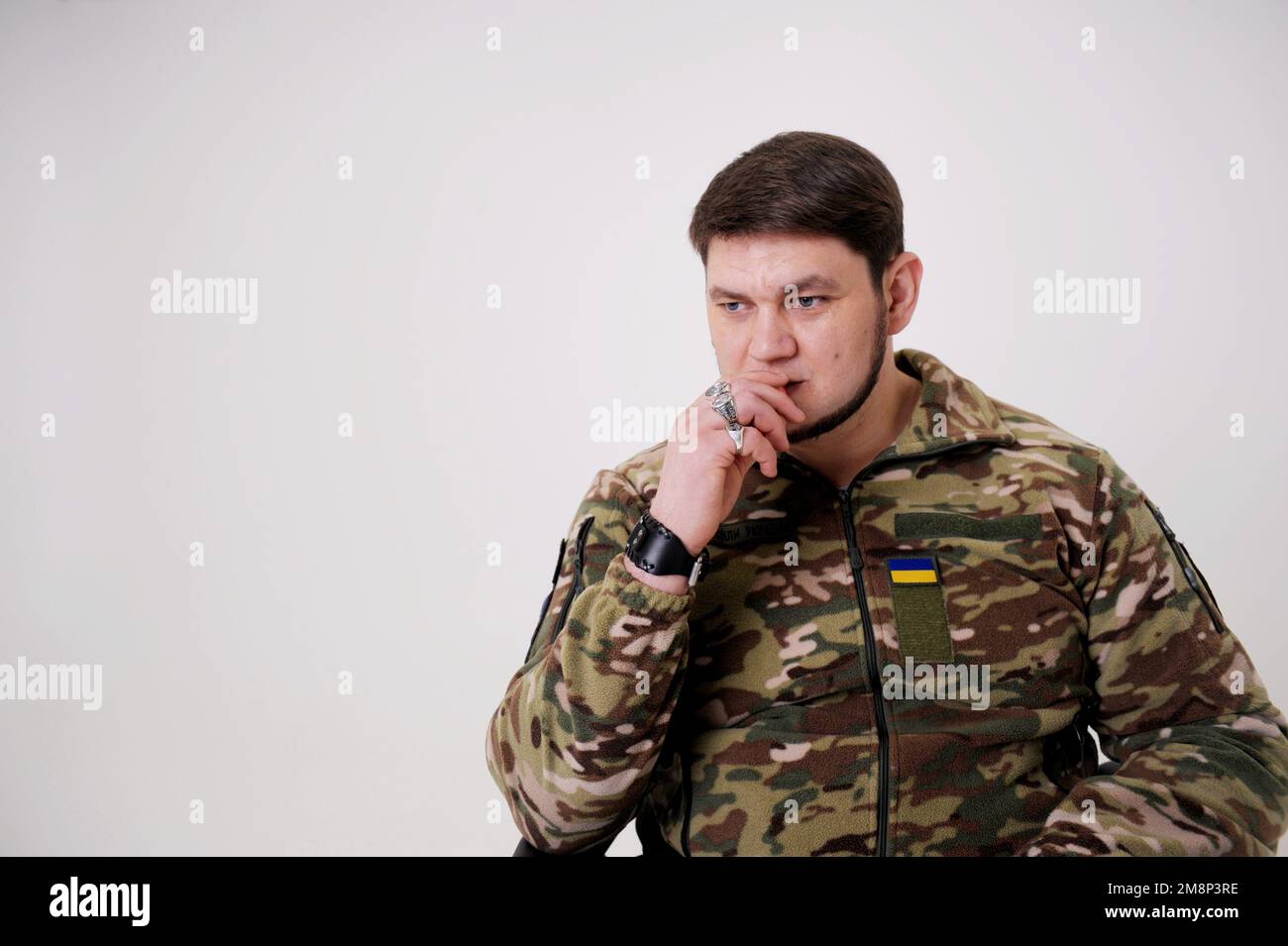 35 Jahre alter, attraktiver Mann des Militärs in Uniform, sitzt und raucht Er hat Ringe an den Fingern Emblem der Ukraine die ukrainische Flagge ist auf Schutzjacke genäht Geschichte der Ukraine Stockfoto