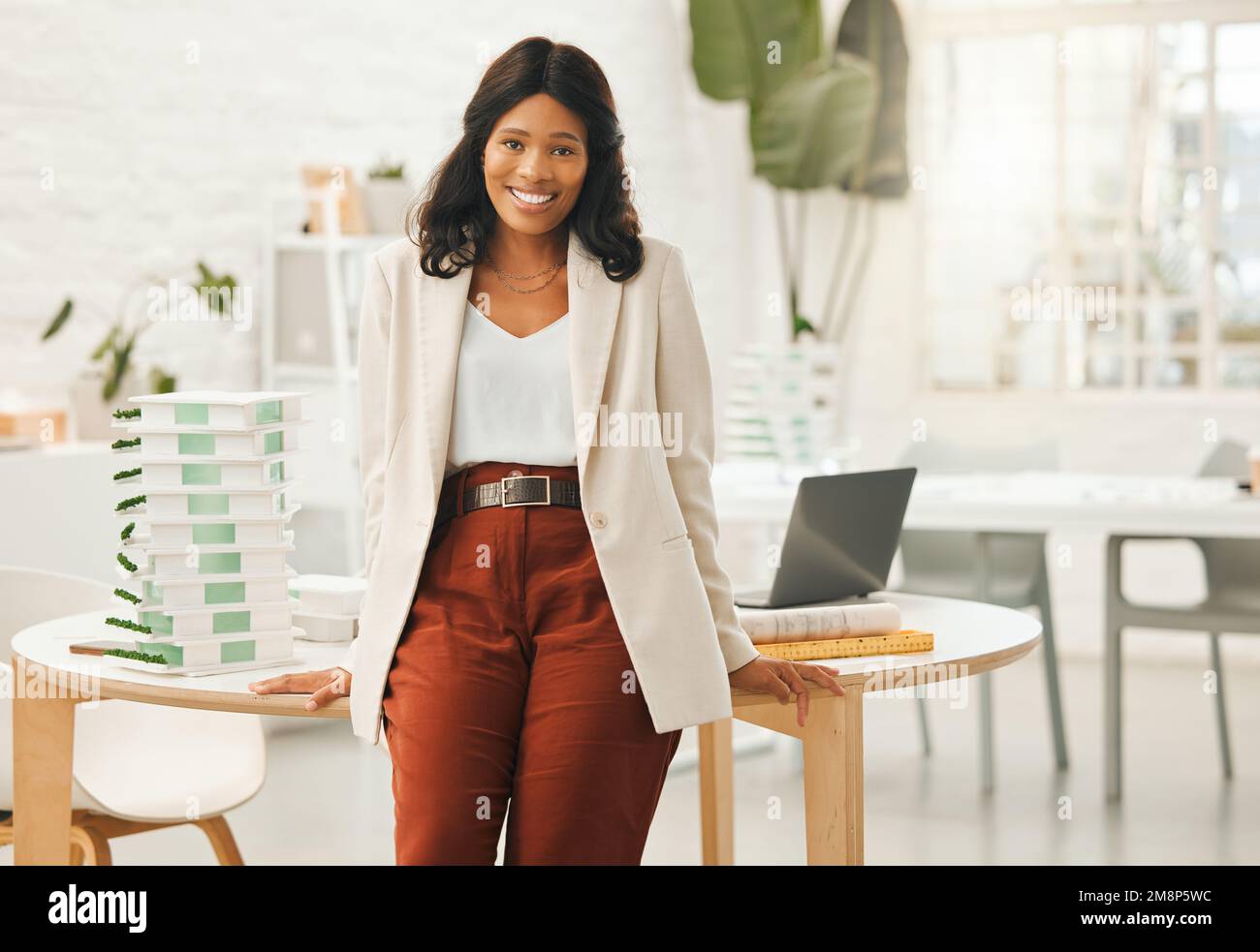 Eine afroamerikanische Geschäftsfrau, die sich auf ihren Schreibtisch lehnt. Porträt einer jungen Geschäftsfrau in ihrem Büro. Kreative Designerin, die in ihrer Agentur arbeitet. Leistungsstark Stockfoto