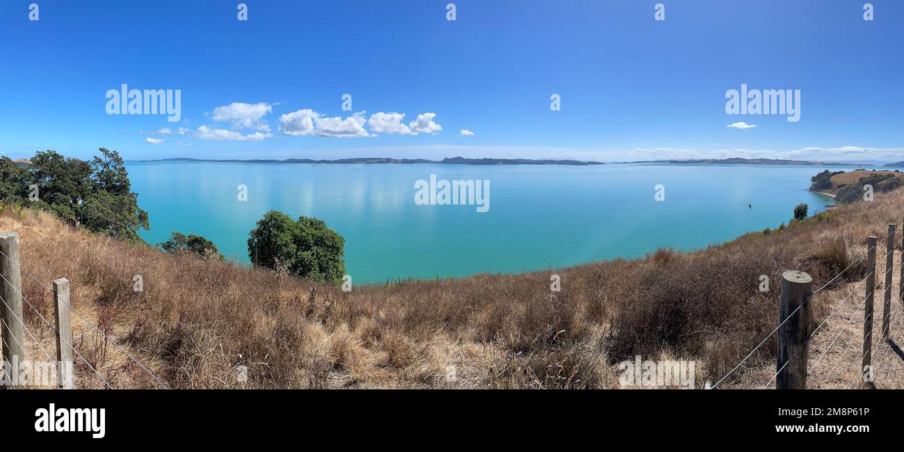 Panoramablick auf die malerische Landschaft mit trockenem Gras, blauem Meer und Bergen im Hintergrund an einem sonnigen Tag, Duder Regional Park, Auckland City, New Z Stockfoto