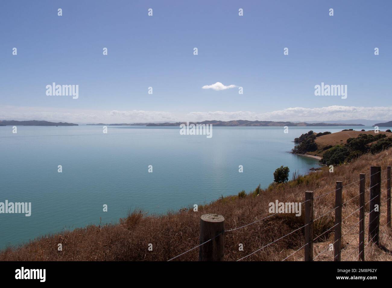 Der Blick auf die malerische Landschaft mit trockenem Grashang, blauem Meer und Bergen im Hintergrund an einem sonnigen Tag, Duder Regional Park, Auckland City, New Z Stockfoto