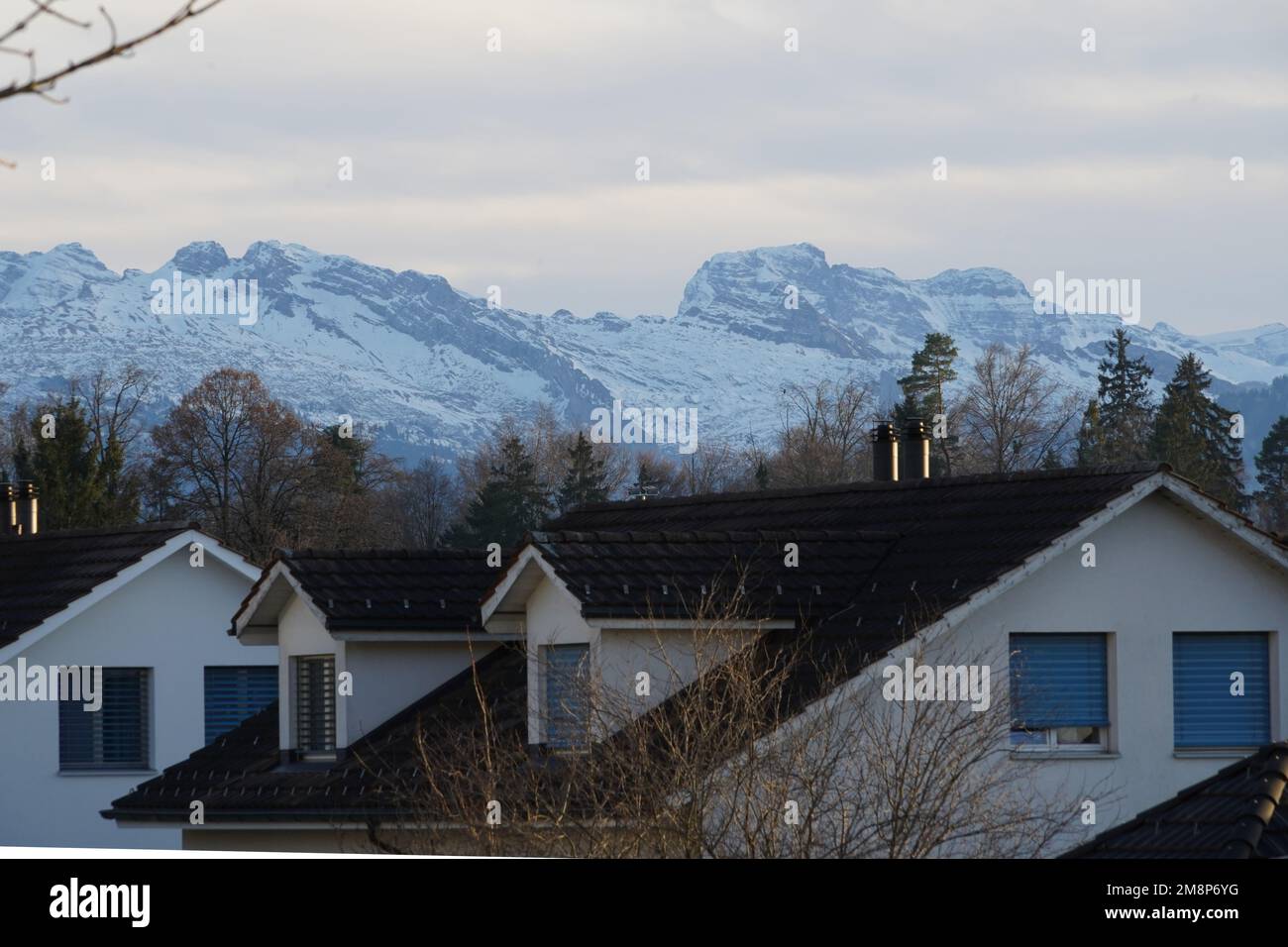 Dächer eines Wohnviertels in einer Schweizer Stadt Hinwil, umgeben von Alpenbergen. Die Berge sind mit Schnee bedeckt. Stockfoto